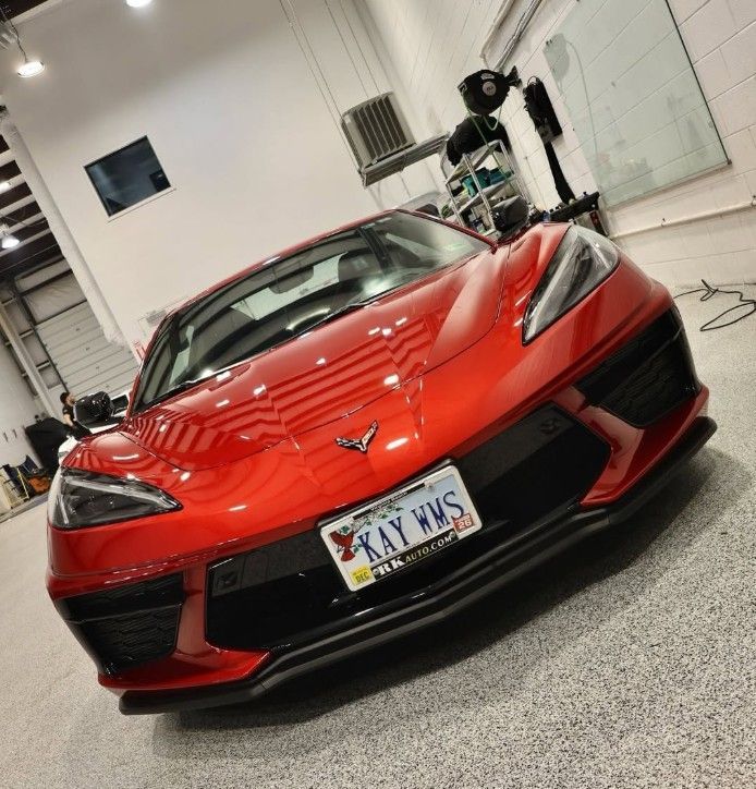 Red Chevrolet Corvette in a garage, with a person cleaning it in the background.
