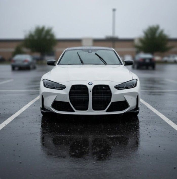White BMW sedan parked in a wet lot, front view, with rain reflections and blurred cars in the background