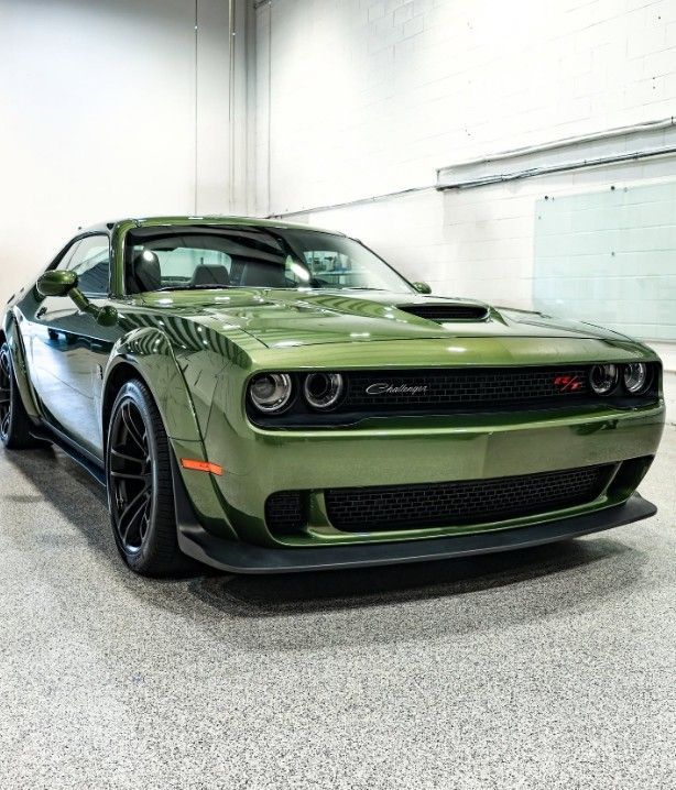 Green Dodge Challenger parked indoors in a white garage, front view