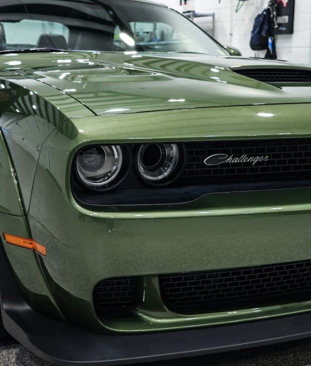 Front view of a green Dodge Challenger in a garage, showing dual round headlights and black grille.