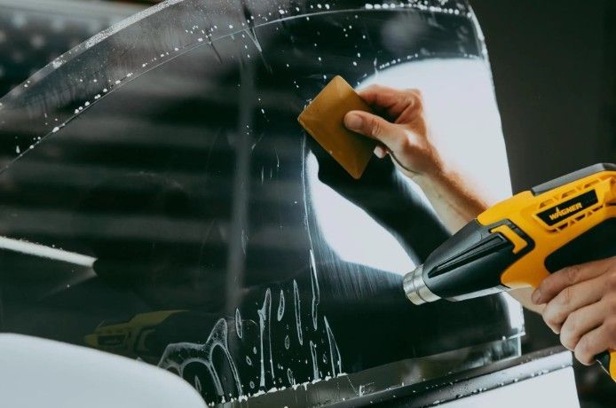Hands cleaning a car window with a squeegee and yellow scraper tool