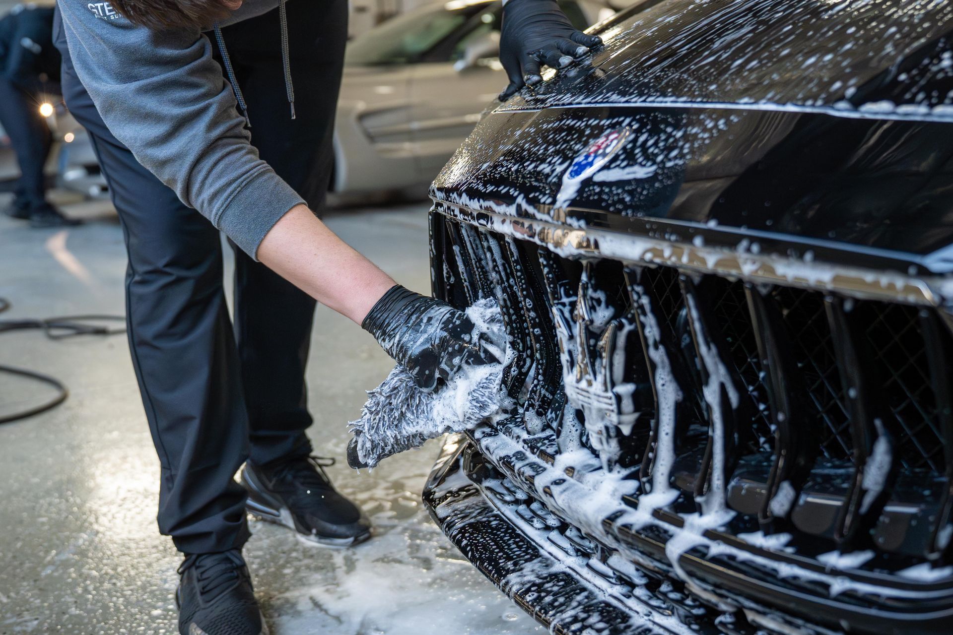 A man is washing a black car with soap and water.