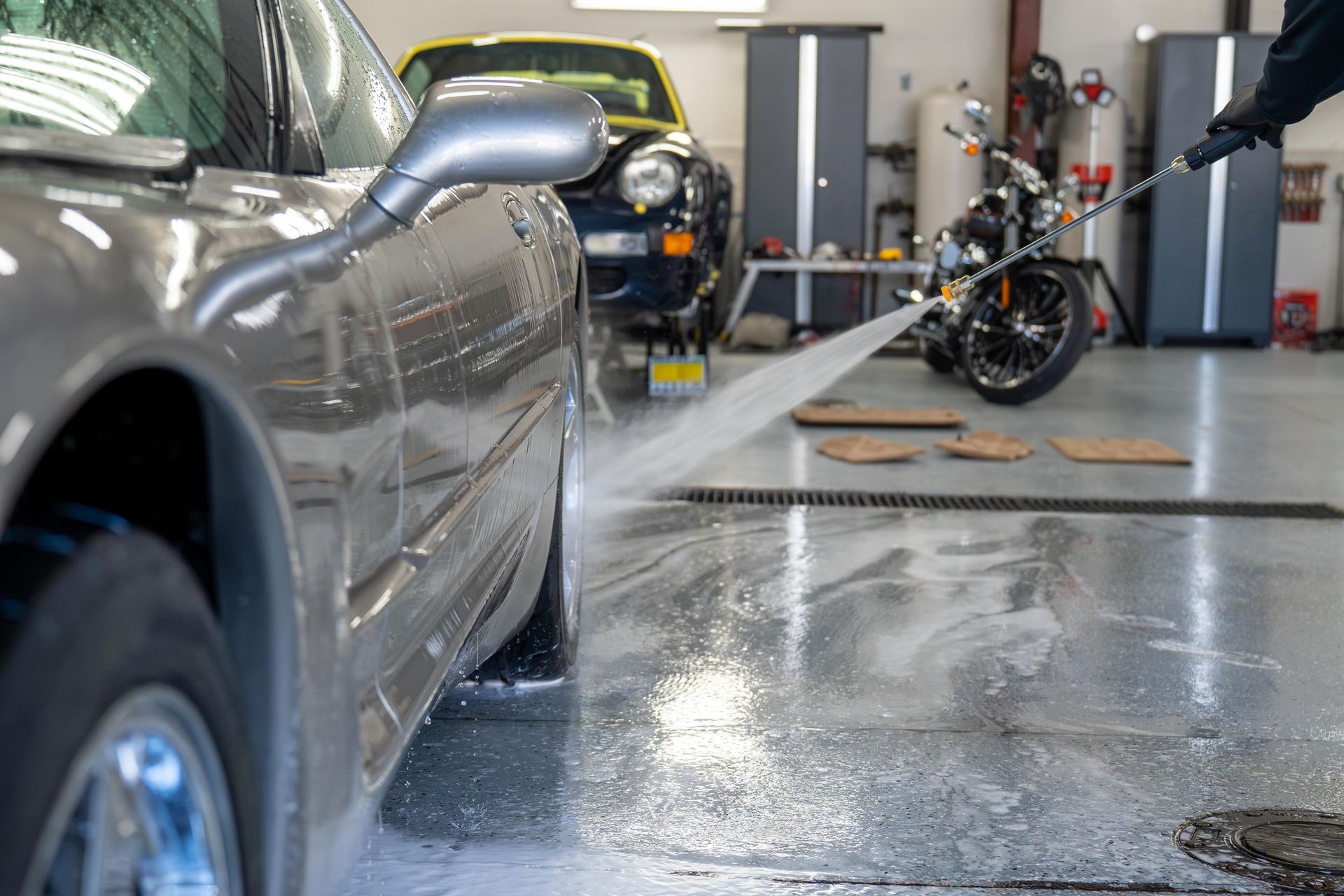 A person is washing a car with a high pressure washer in a garage.