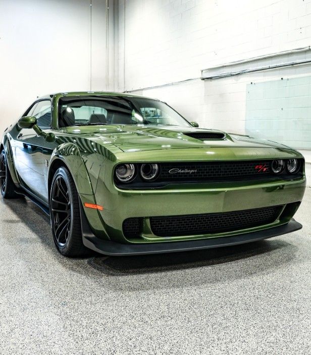 Green Dodge Challenger parked indoors on a showroom floor, front three-quarter view