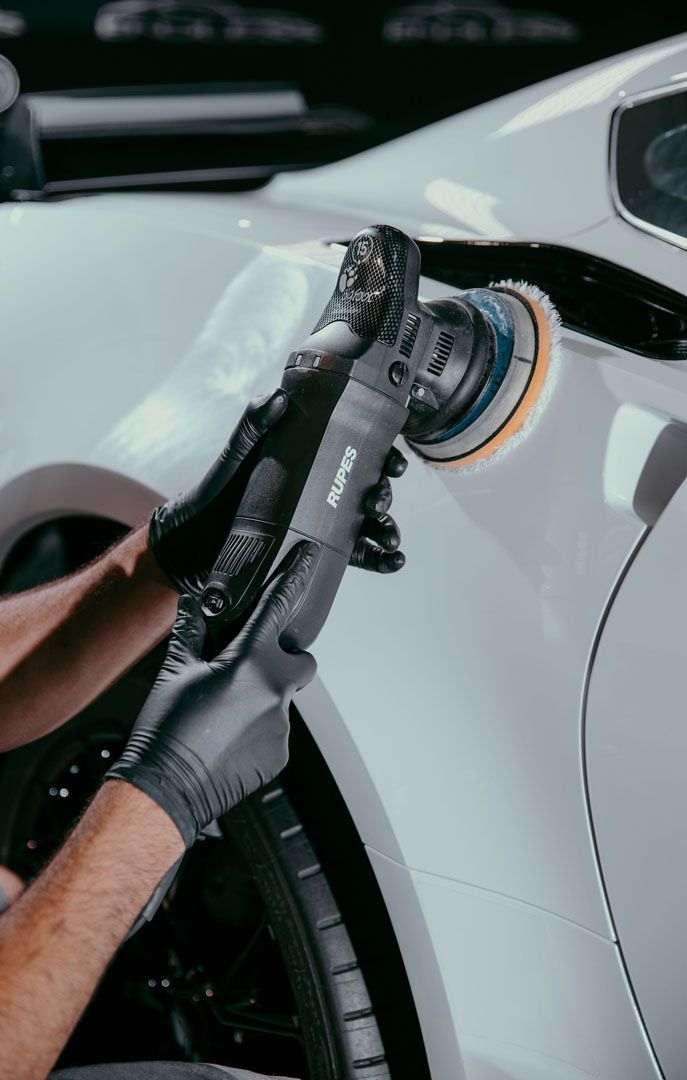 A man is polishing a white car with a machine.