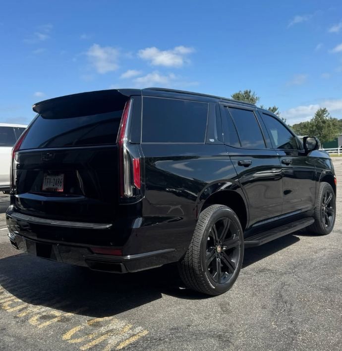 Black SUV parked in a lot, viewed from the rear side under a bright blue sky.