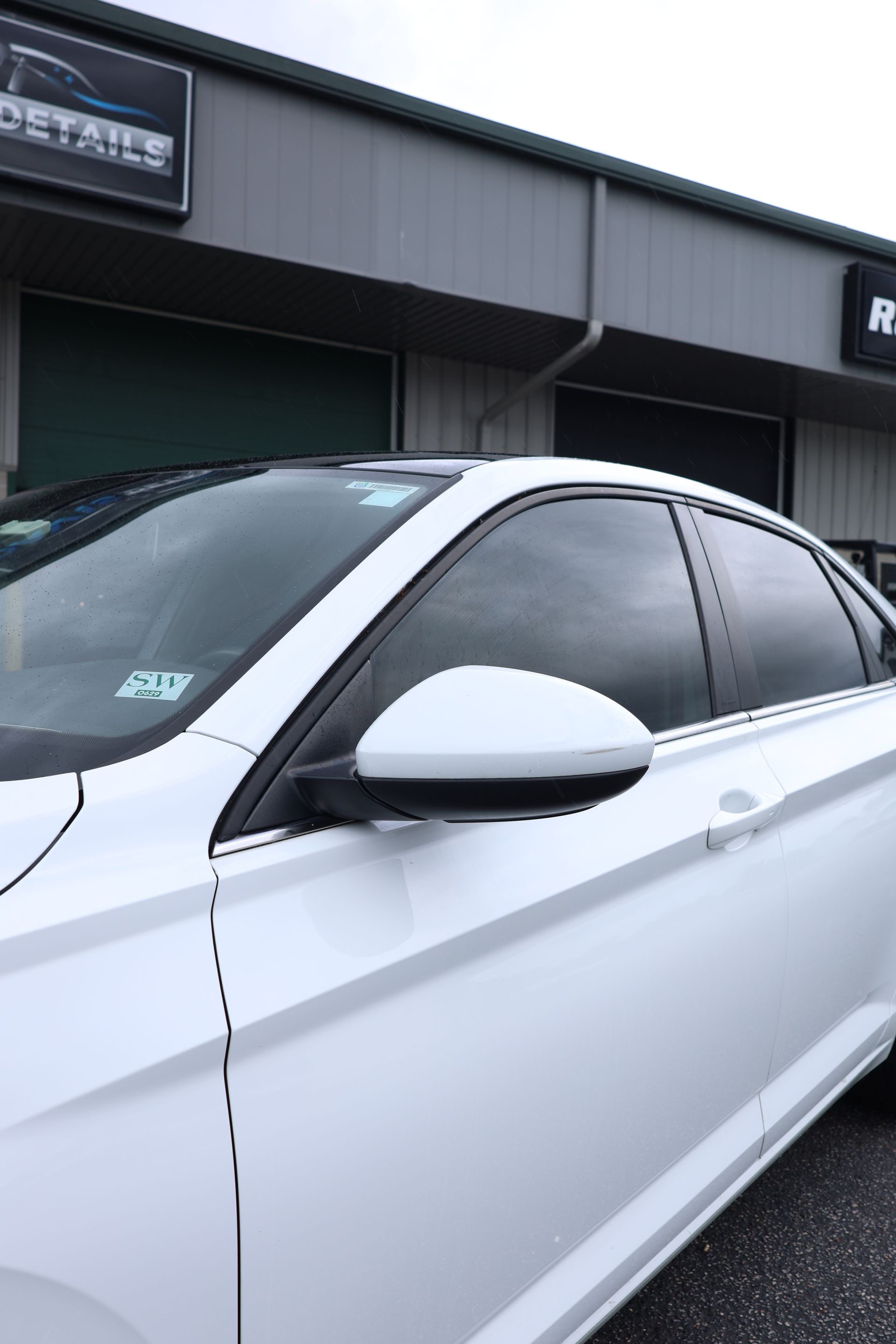 White car parked outside a building with dark windows and a silver side mirror