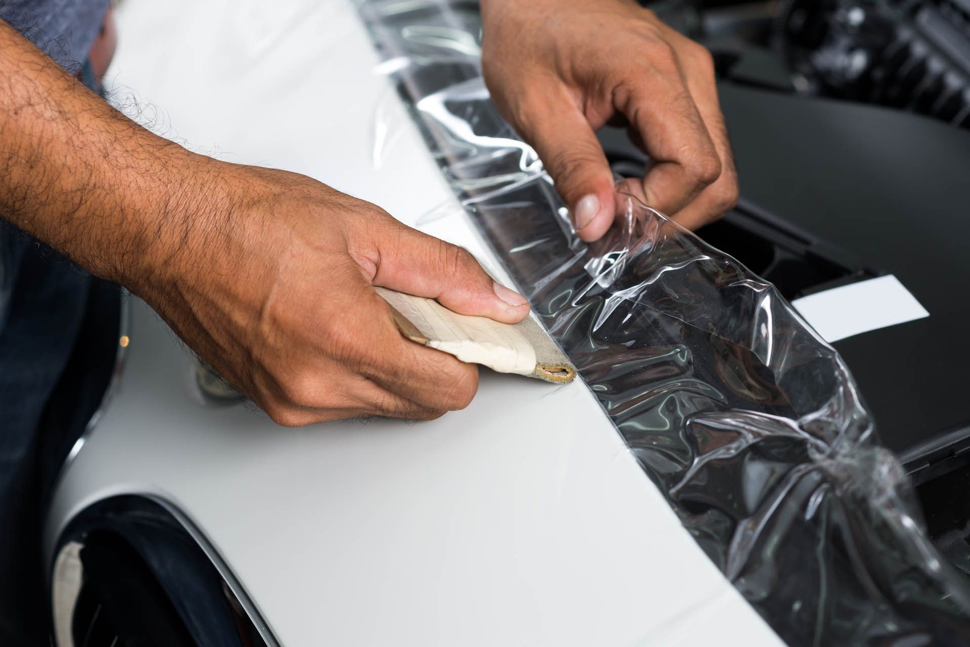 A man is applying plastic wrap to a car fender.