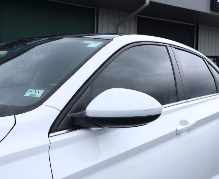 White car with tinted windows and silver side mirror parked by a building