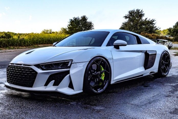 White Audi R8 sports car with black accents and lime green brake calipers parked on wet asphalt.