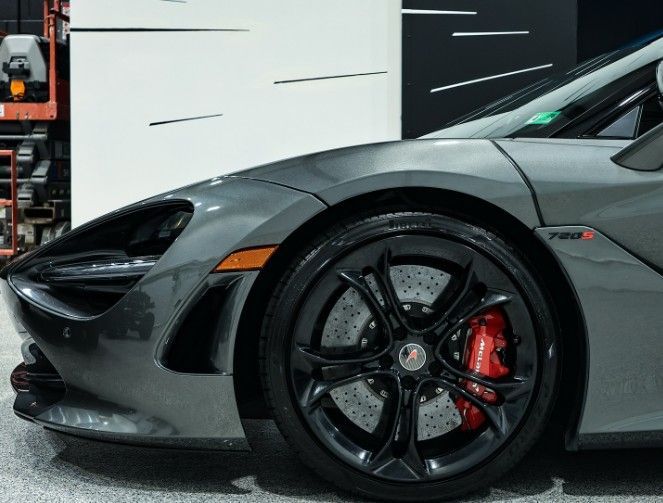 Gray McLaren sports car front wheel, black rim, red brake caliper.