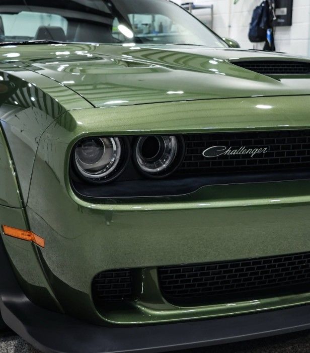 Green Dodge Challenger front end parked indoors, showing the grille and headlights.