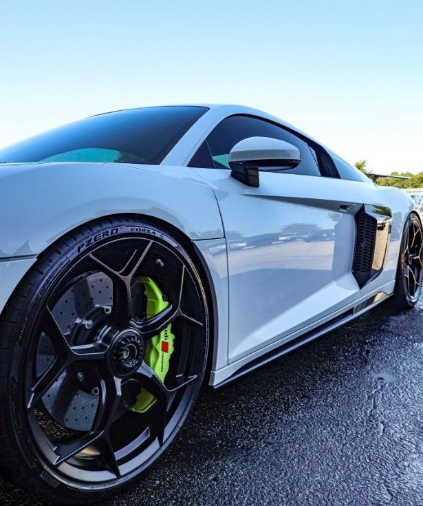 White sports car with black rims and neon green brake calipers parked on a road under a blue sky