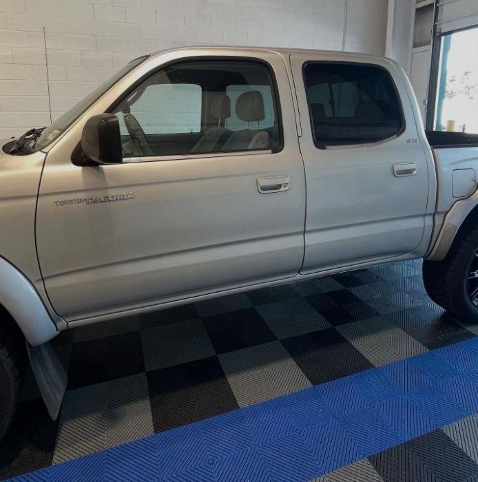 Silver pickup truck parked indoors on black-and-gray checkered flooring near a blue ramp.