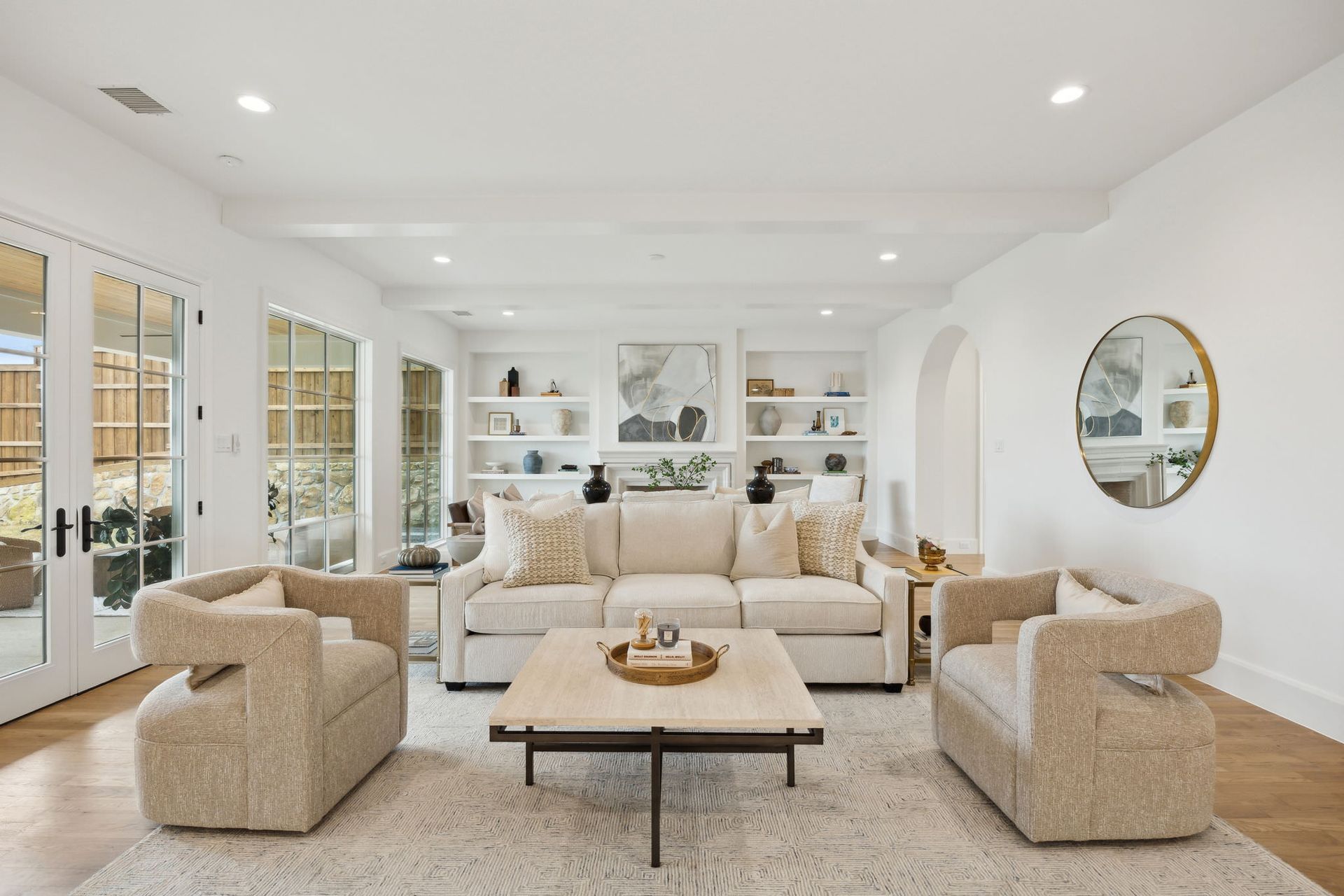 Living room with white walls, built-in shelves, sofa, two armchairs, coffee table, and large windows.