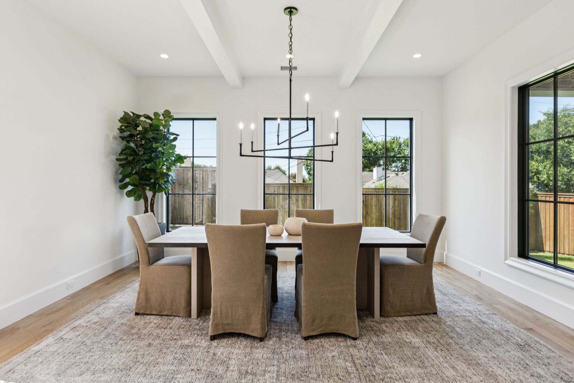 Dining room with table and chairs under a chandelier, with large windows and a rug.