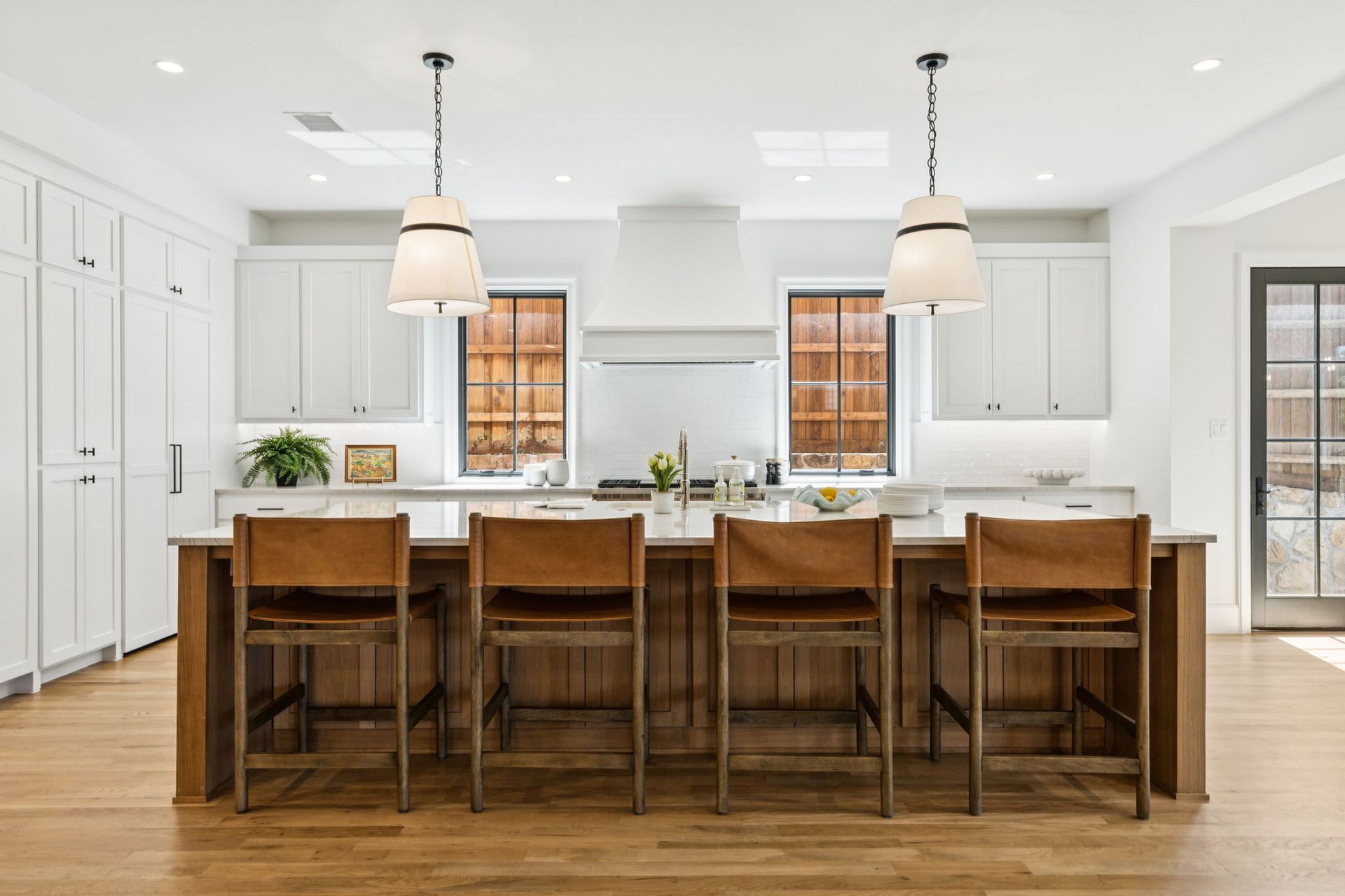 Spacious white kitchen with wooden island, brown leather bar stools, and pendant lights.