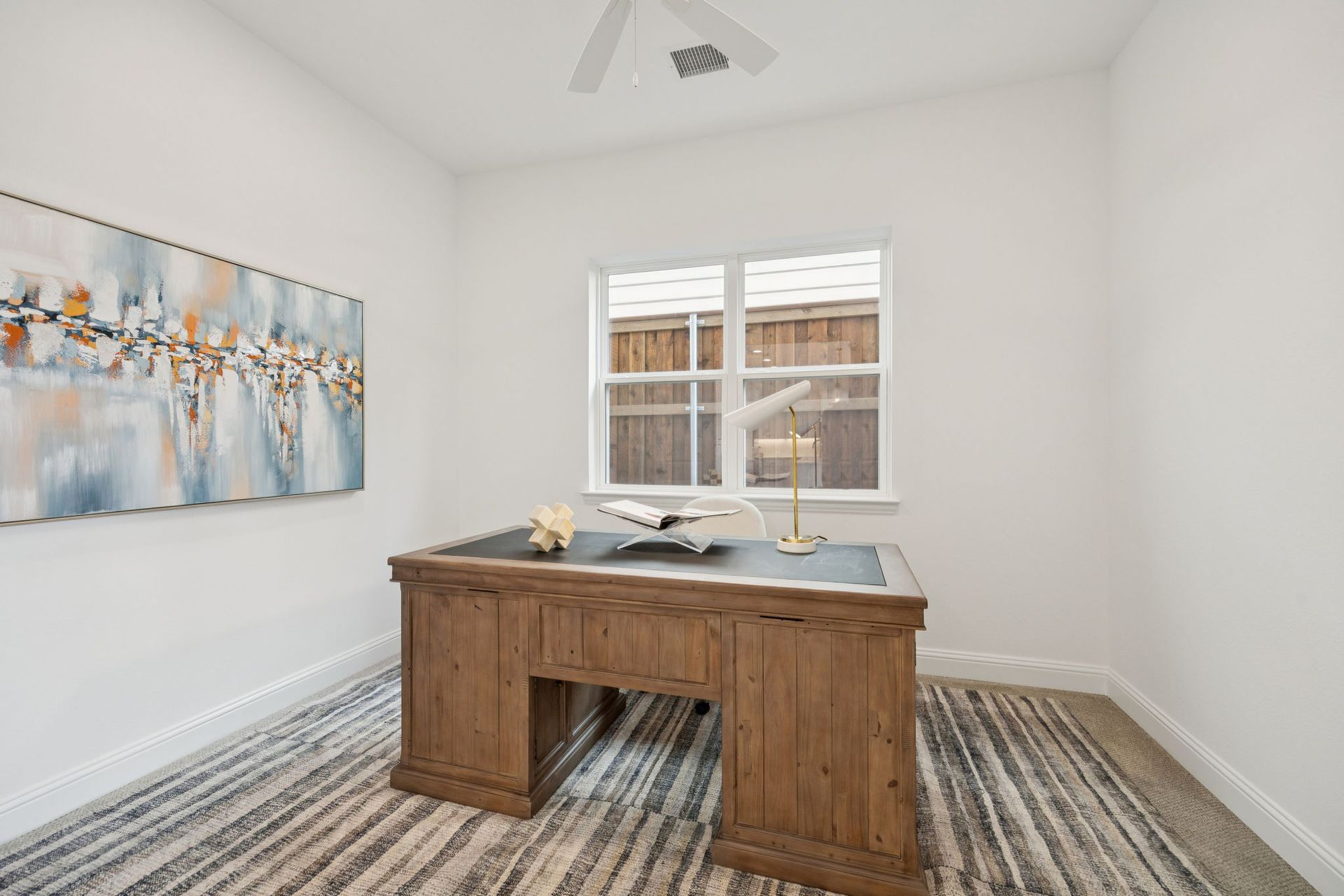 Home office with wooden desk, artwork, and window.