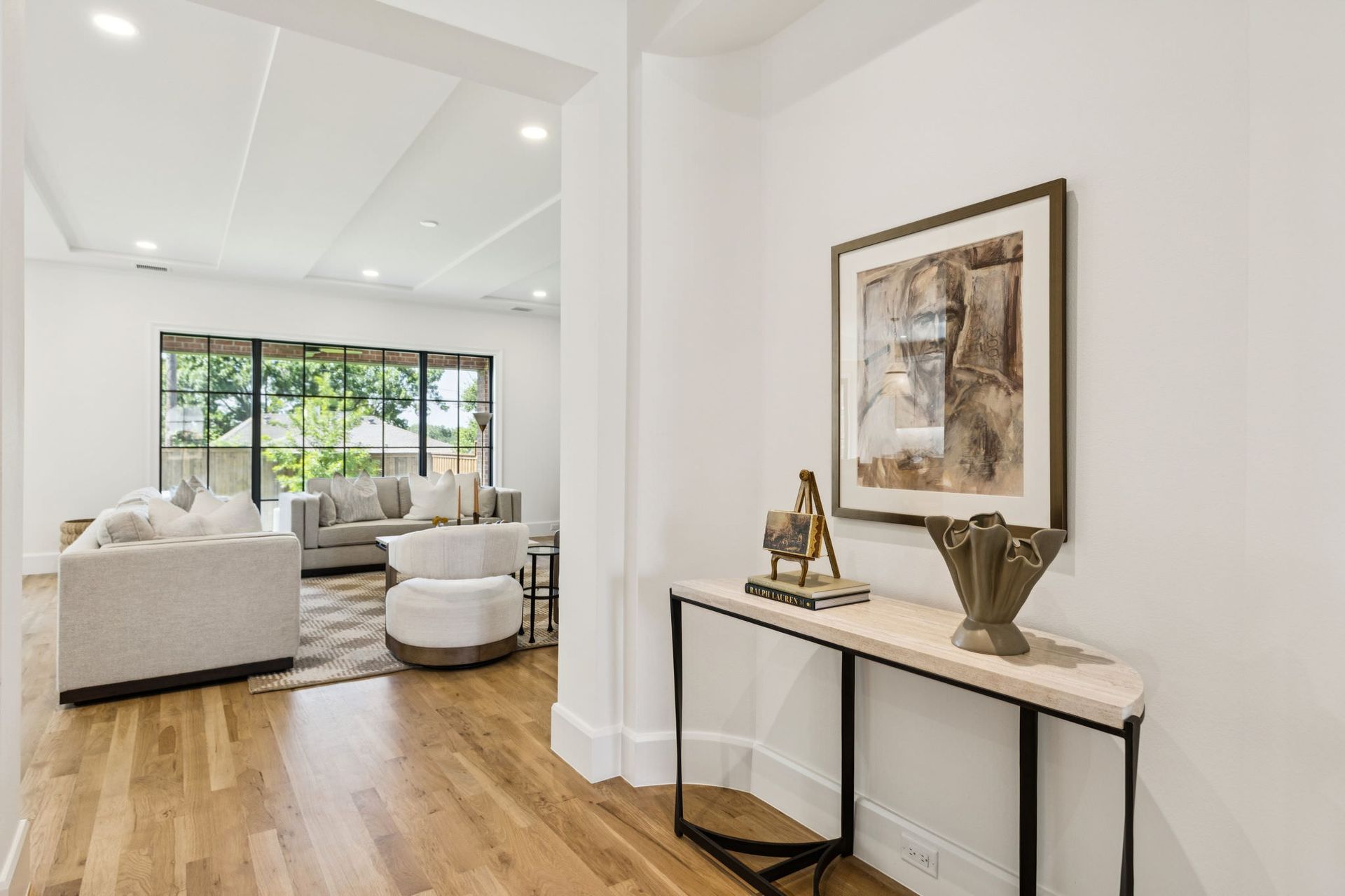 Hallway with a console table, artwork, and view into a living room with couches and natural light.