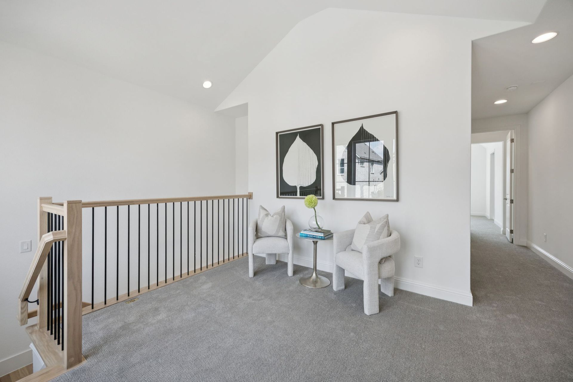 Hallway with carpet, two chairs, artwork, and a railing.