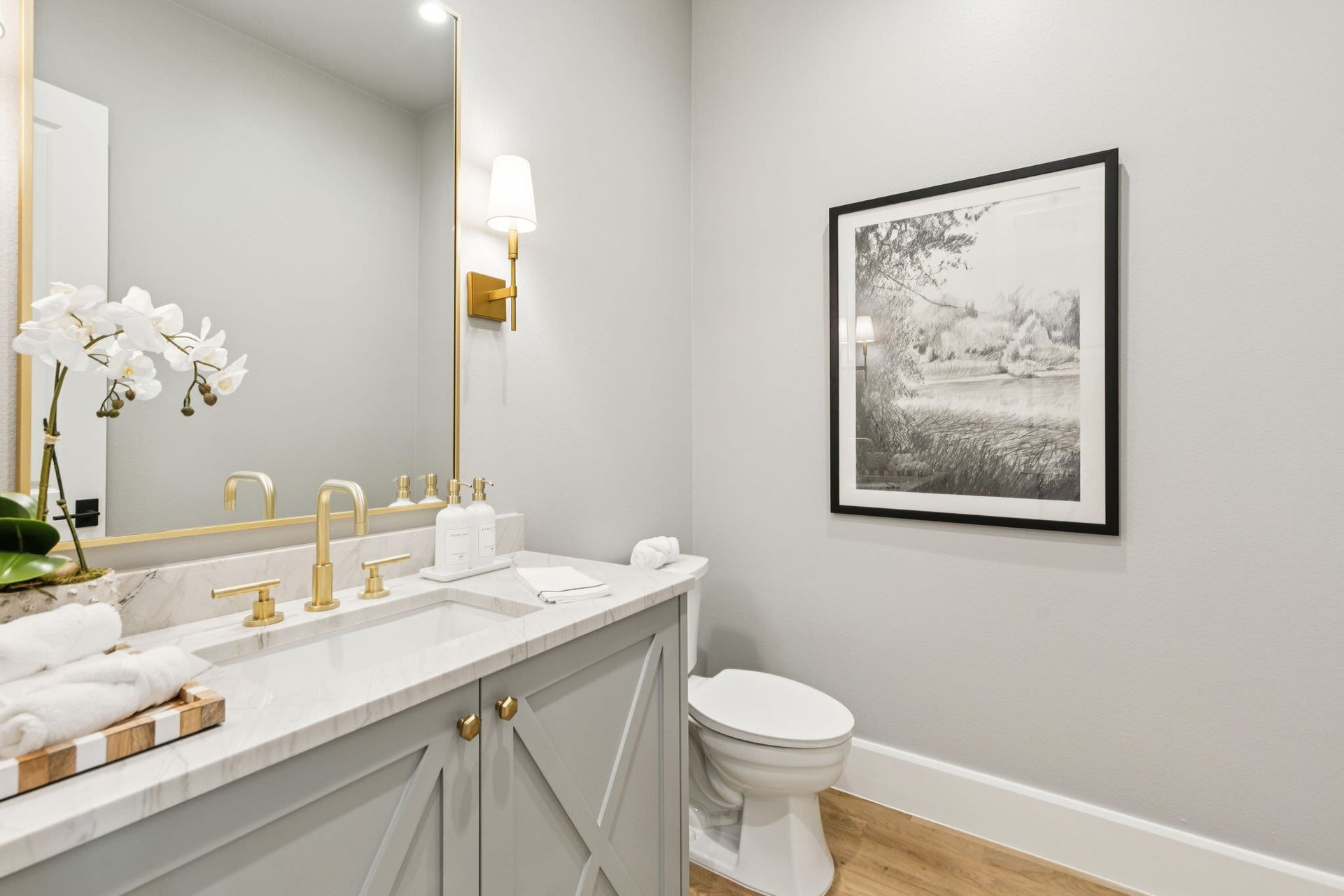 Powder room with light gray walls, gold accents, marble vanity, and framed art.