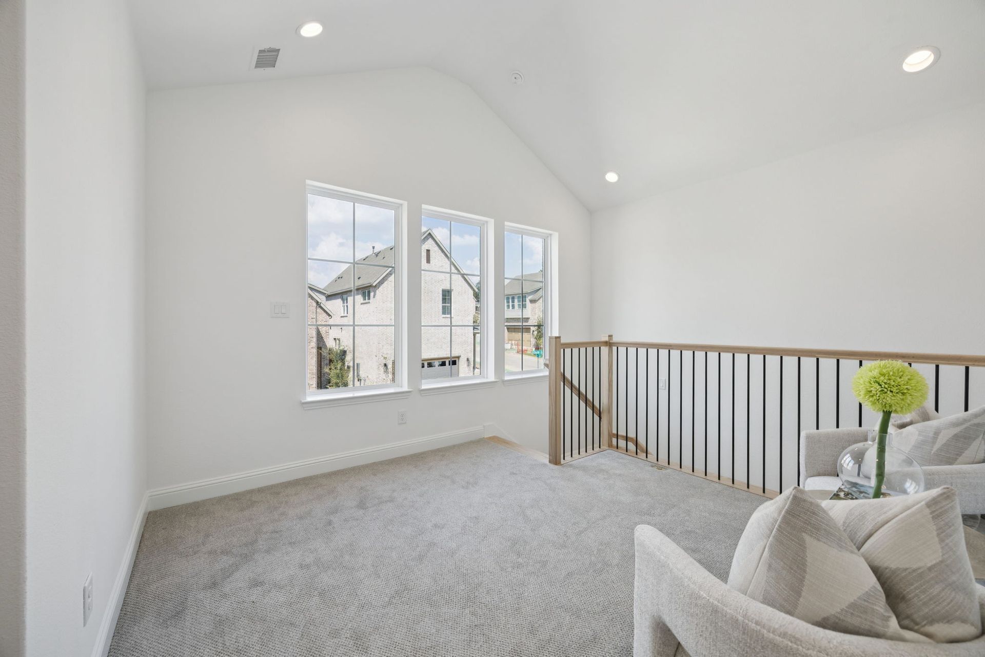 Bright loft area with three windows, gray carpet, and two armchairs. A light railing leads to the lower level.