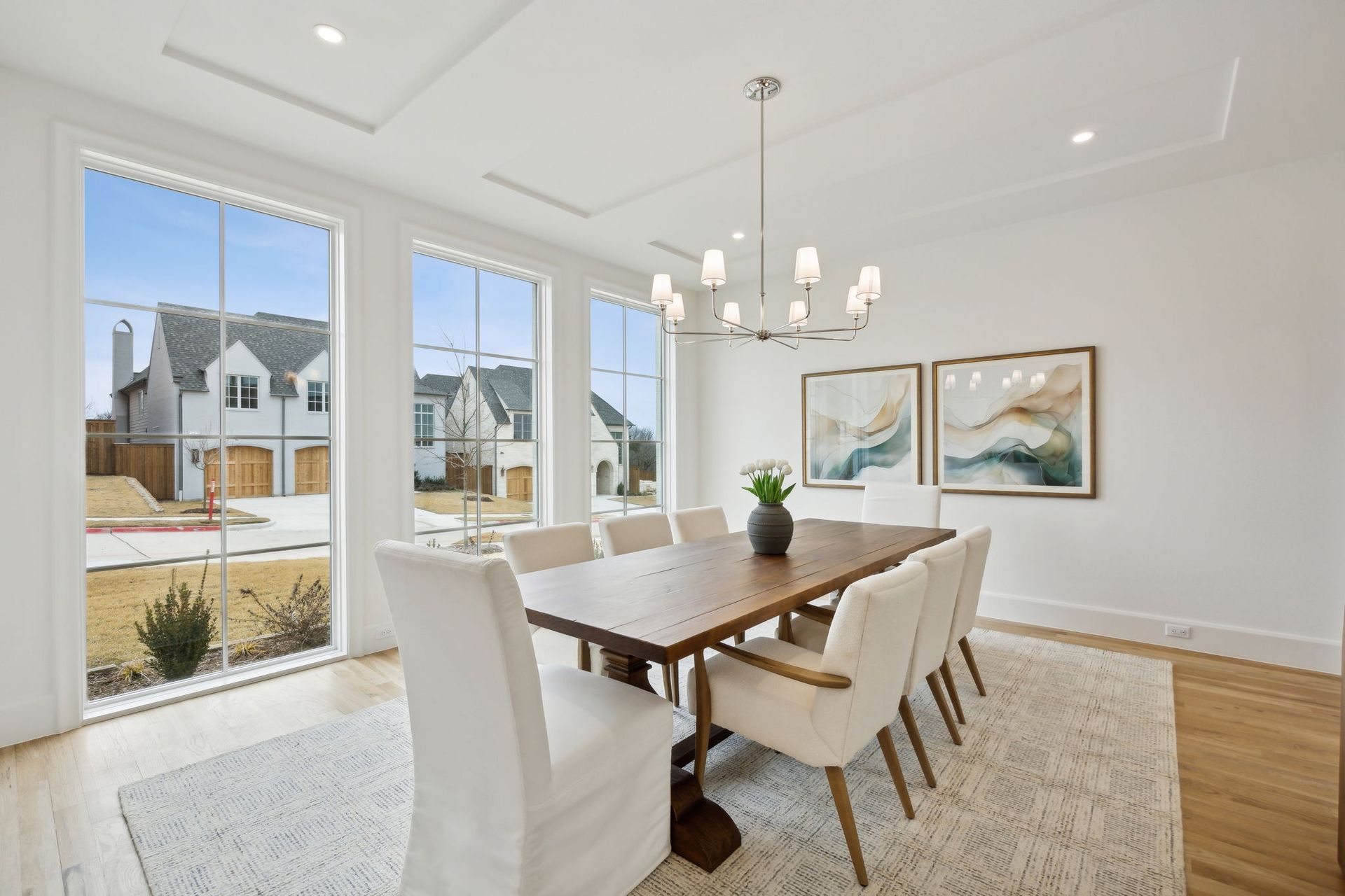 Dining room with large windows, table set for ten, chandelier, and artwork.