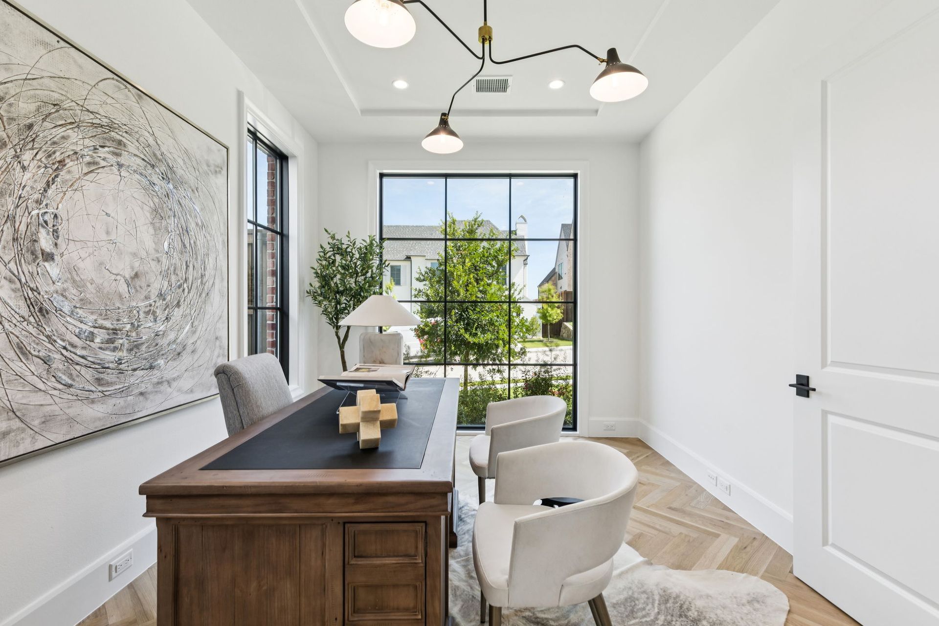 Office with large window, desk, chairs, artwork, and modern light fixture.
