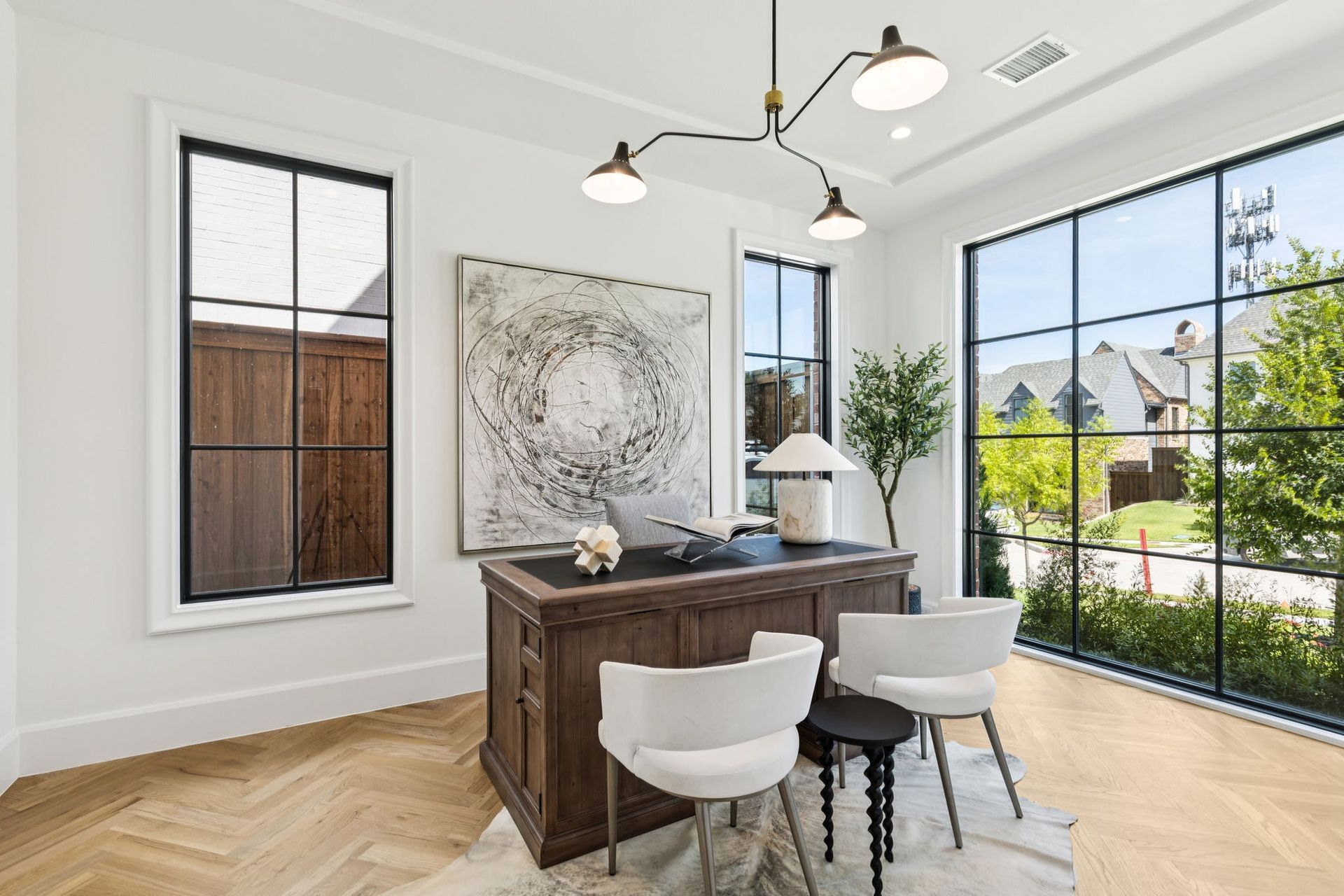 A bright home office with large windows, dark wood desk, and white chairs.