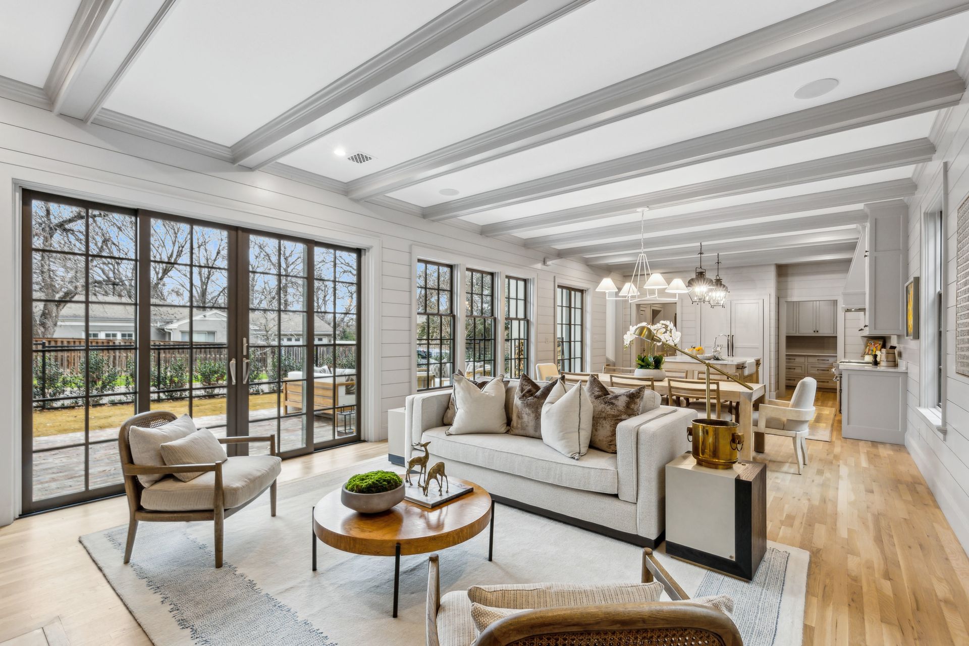 Bright living room with large windows, white walls, wood beams, and light wood flooring.