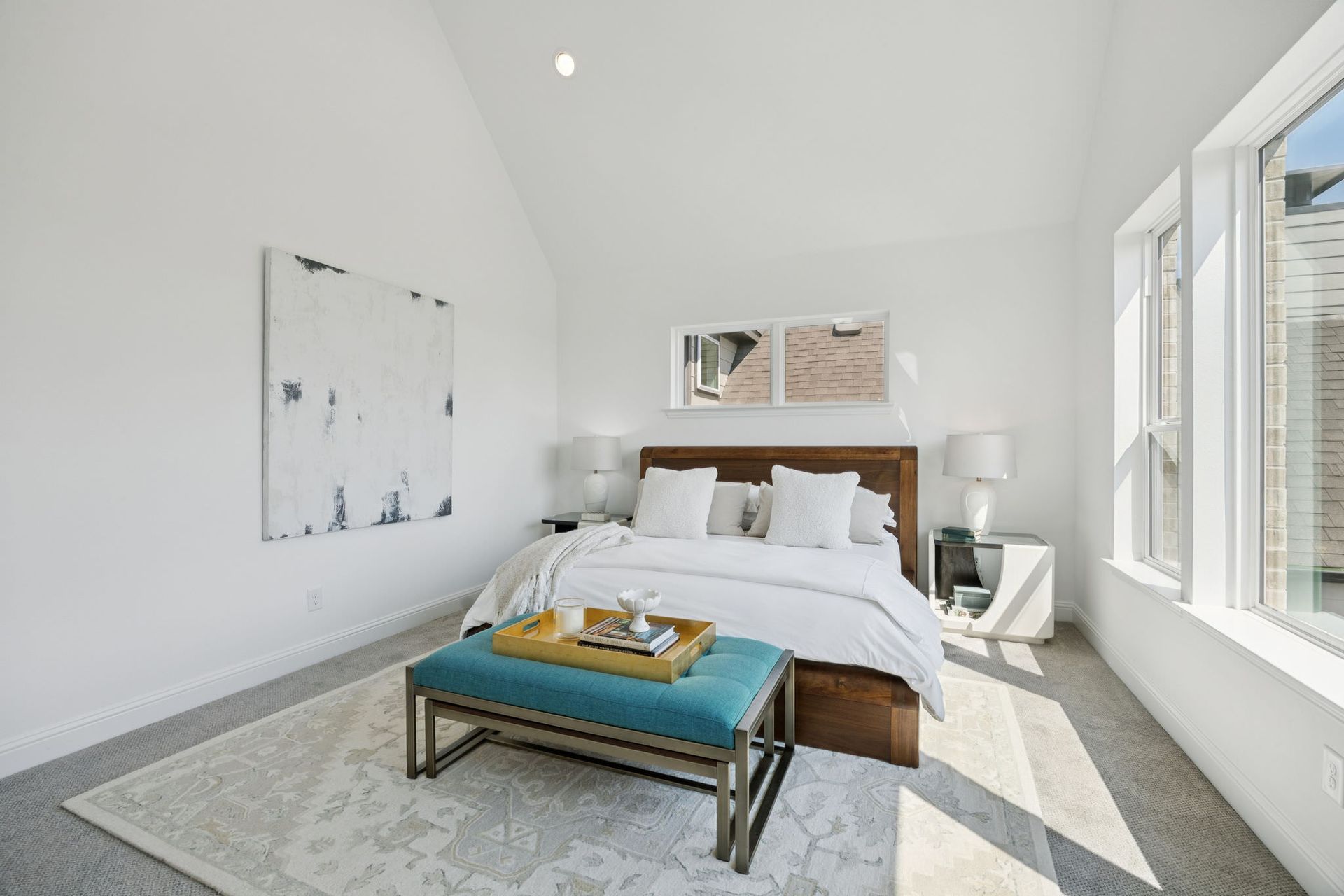 Bedroom with white walls, a bed with white linens, turquoise bench, and sunlight through a window.