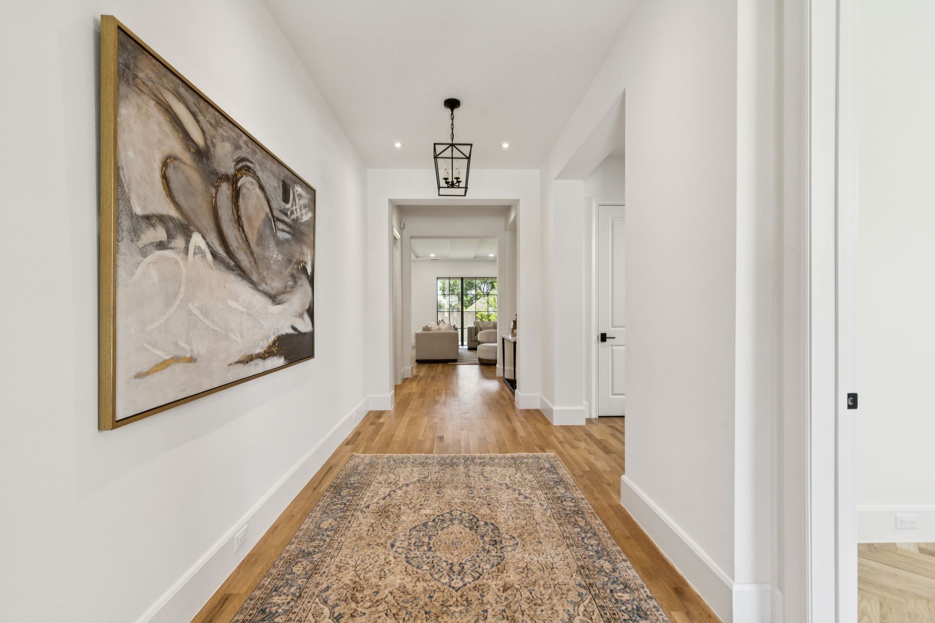 Hallway with hardwood floors, white walls, art, and patterned rug.