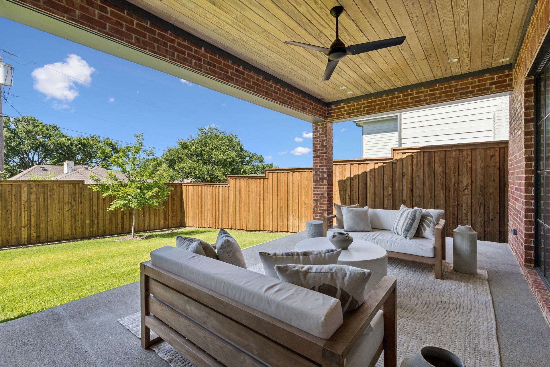 Outdoor patio with seating area, wooden fence, brick accents, and blue sky.