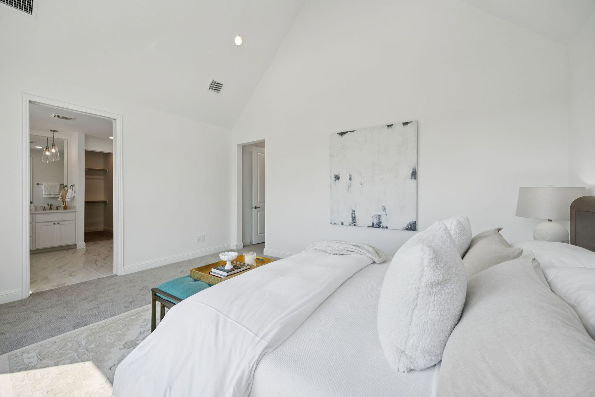 Bedroom with high ceiling, white walls, and a bed with white bedding, and a light-colored rug.
