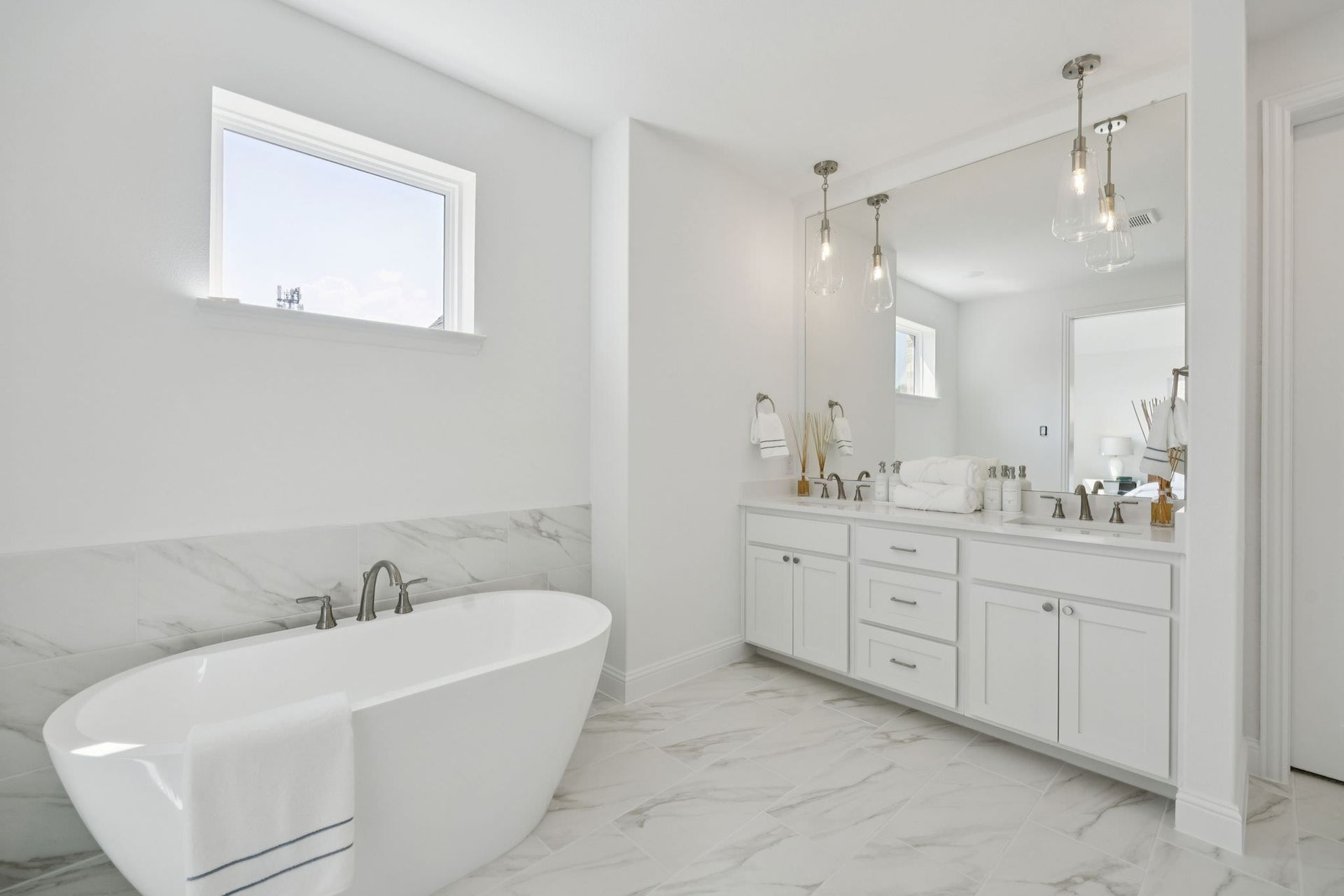 White bathroom with a soaking tub and vanity, marble floor, large mirror, and window.