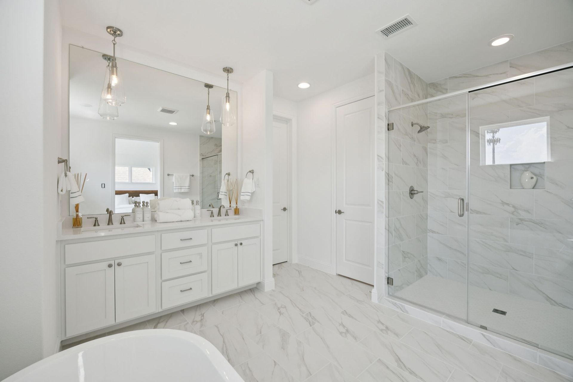 White bathroom with a marble shower, vanity with mirror, and a standalone tub.