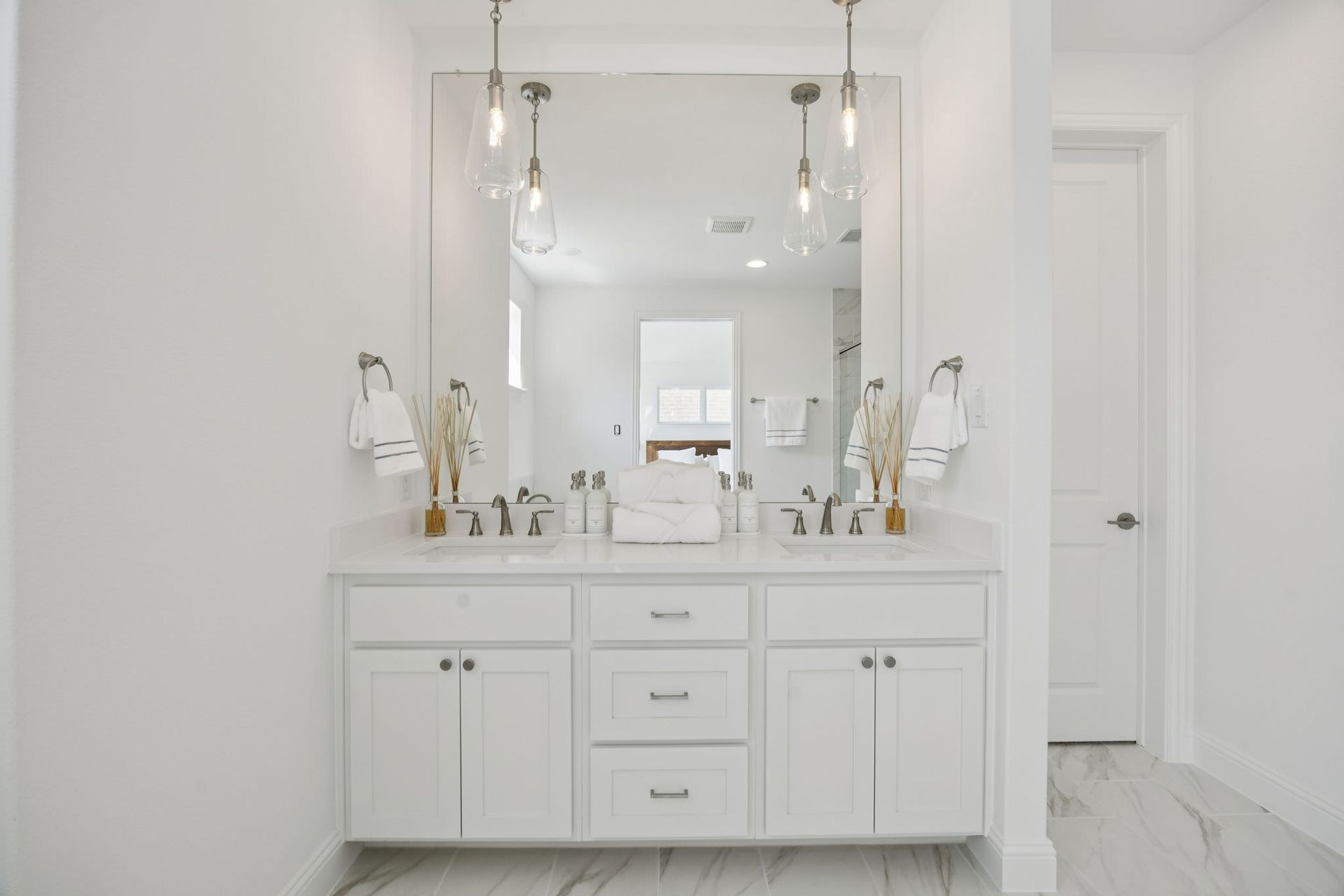 White bathroom with a double vanity, large mirror, and hanging lights.