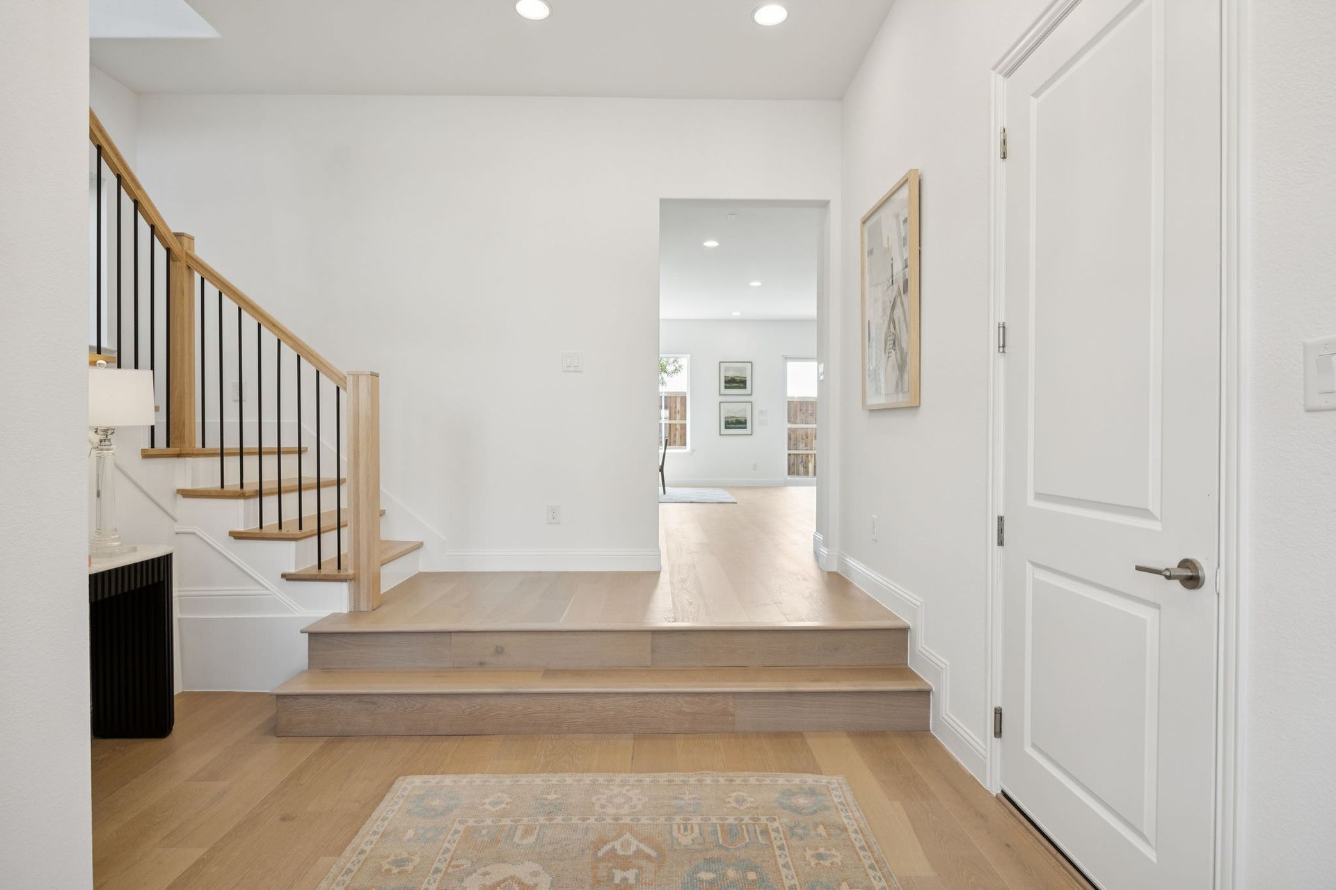 Entryway with staircase, light wood floors, white walls, and a view into the next room.