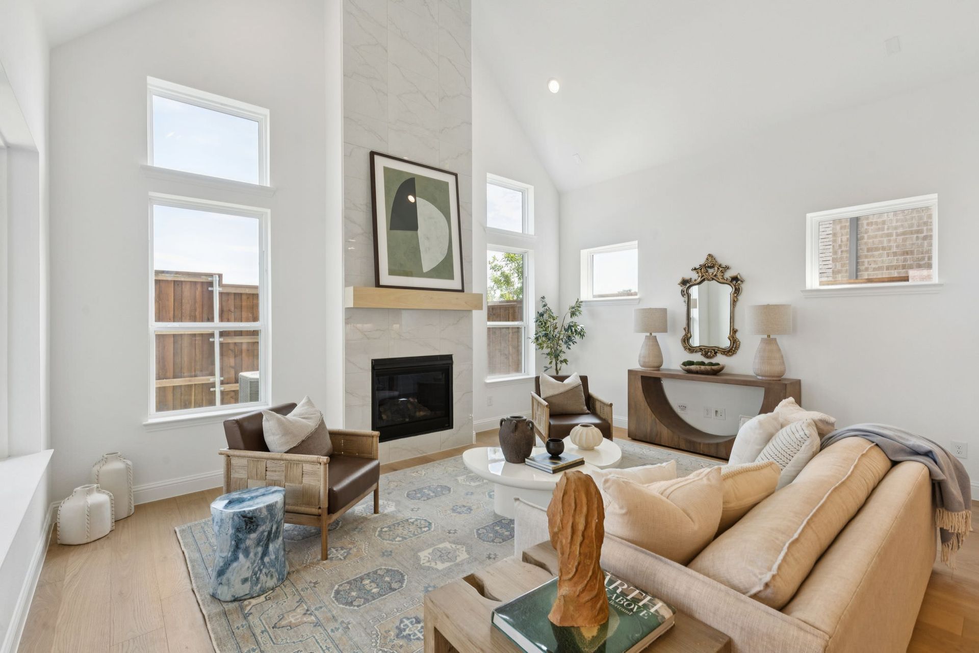 Bright living room with fireplace, beige sofa, wooden floors, and large windows.