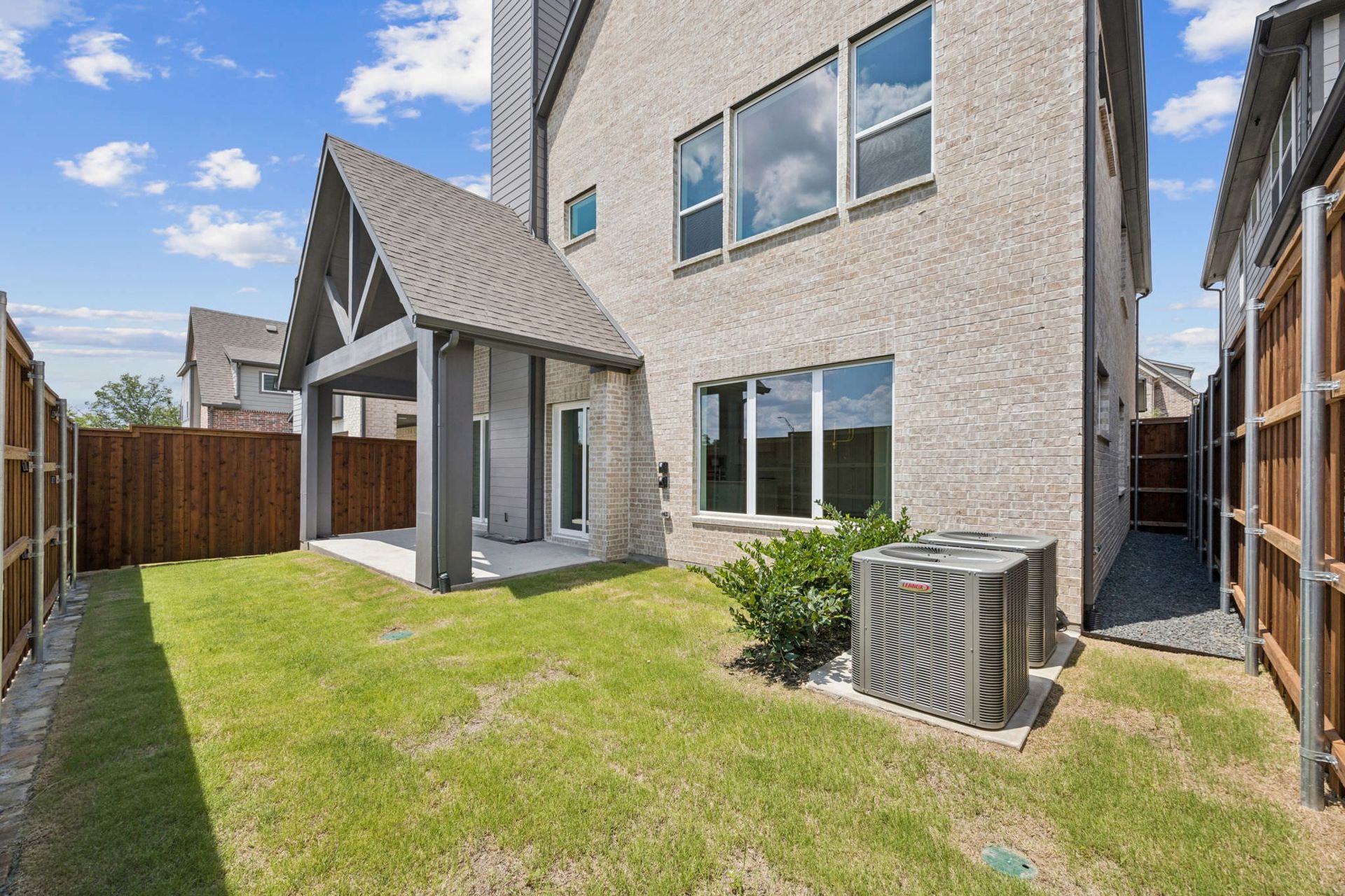 Backyard of a two-story brick home with a covered patio, green grass, and wooden fence.
