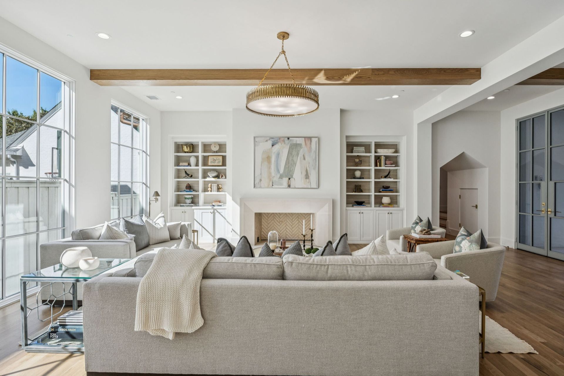 Bright, airy living room with large windows, light gray furniture, fireplace, and wood beams.