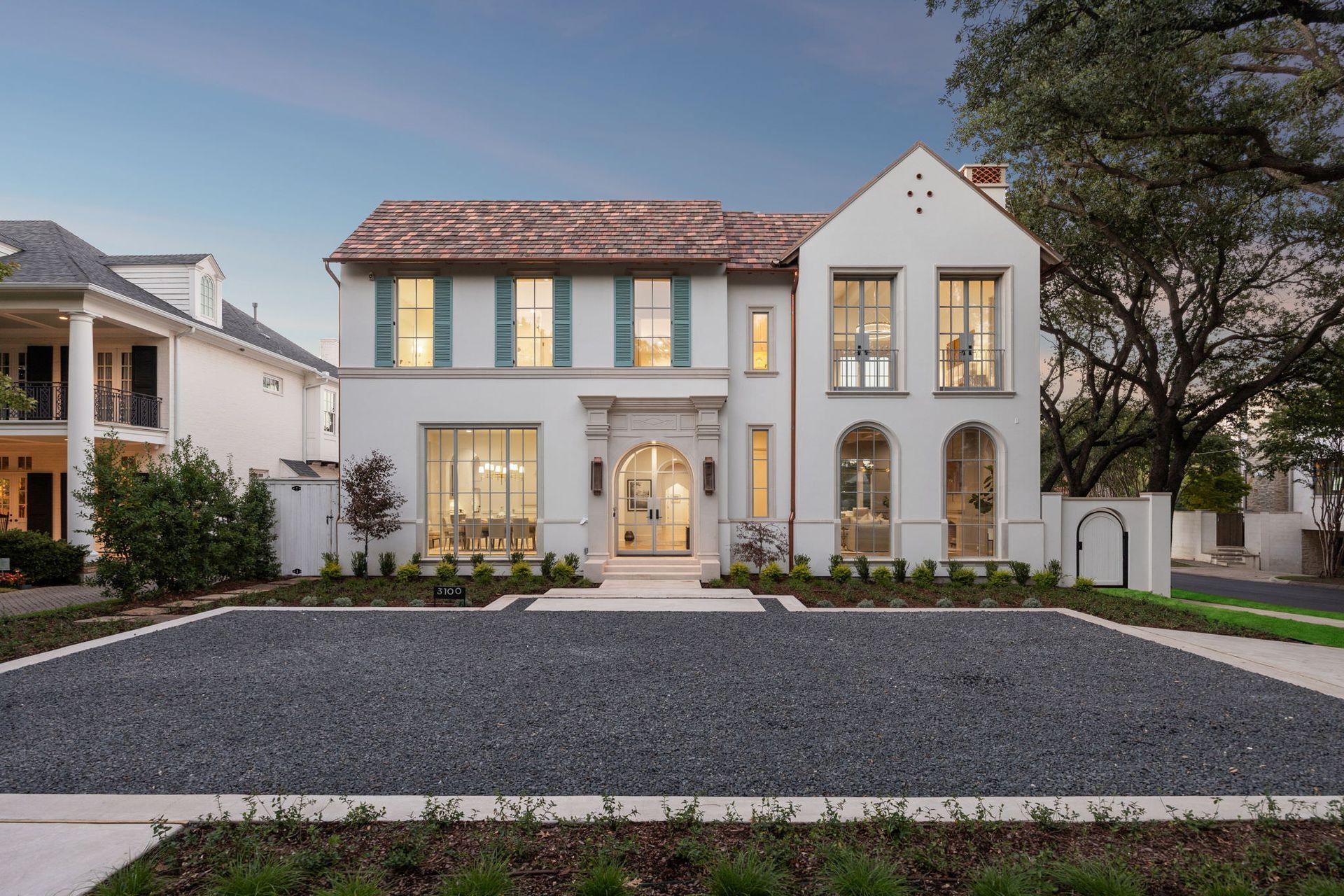 White stucco house with clay tile roof and gravel driveway.