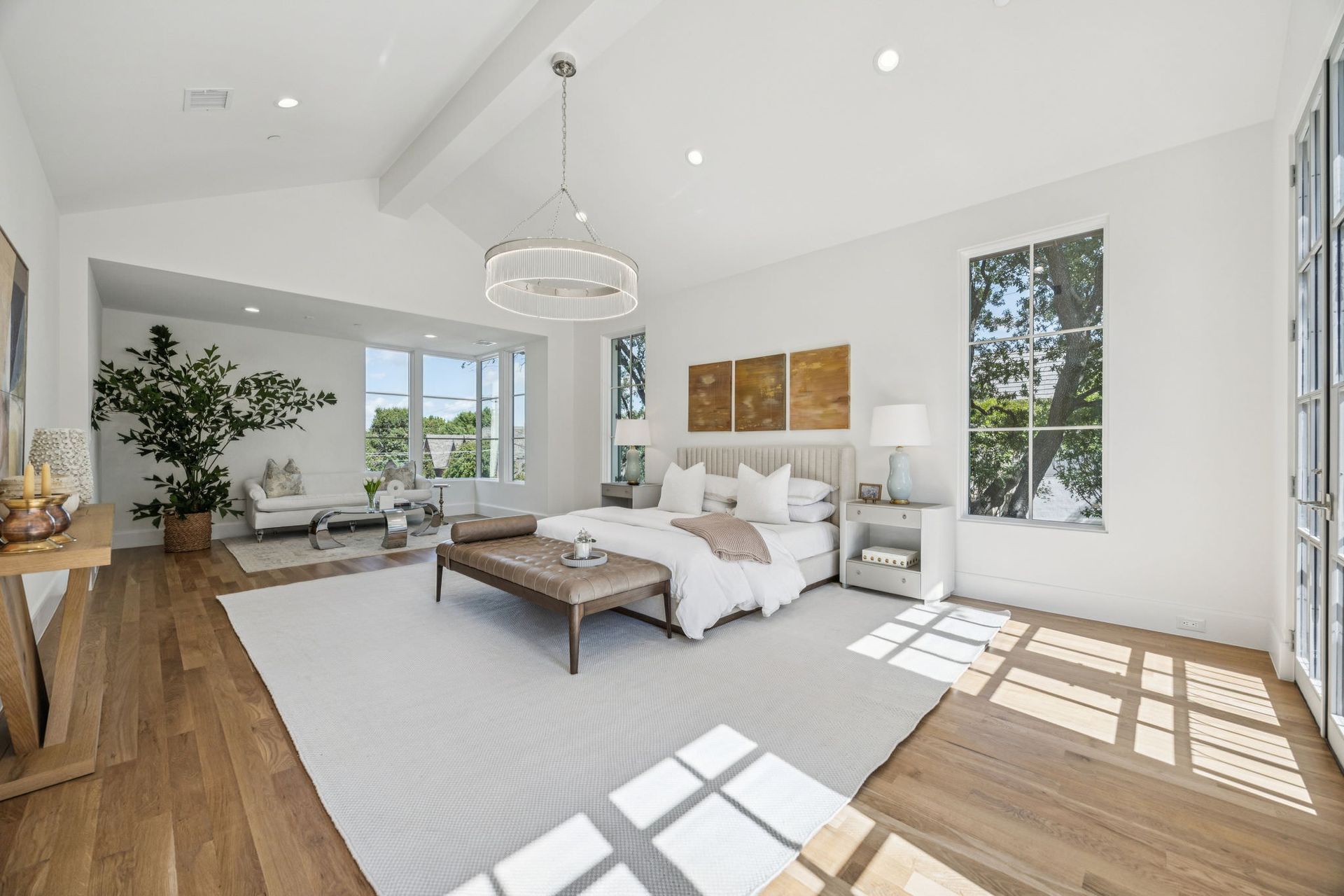Spacious white bedroom with hardwood floors, a large bed, and a sitting area with bright natural light.