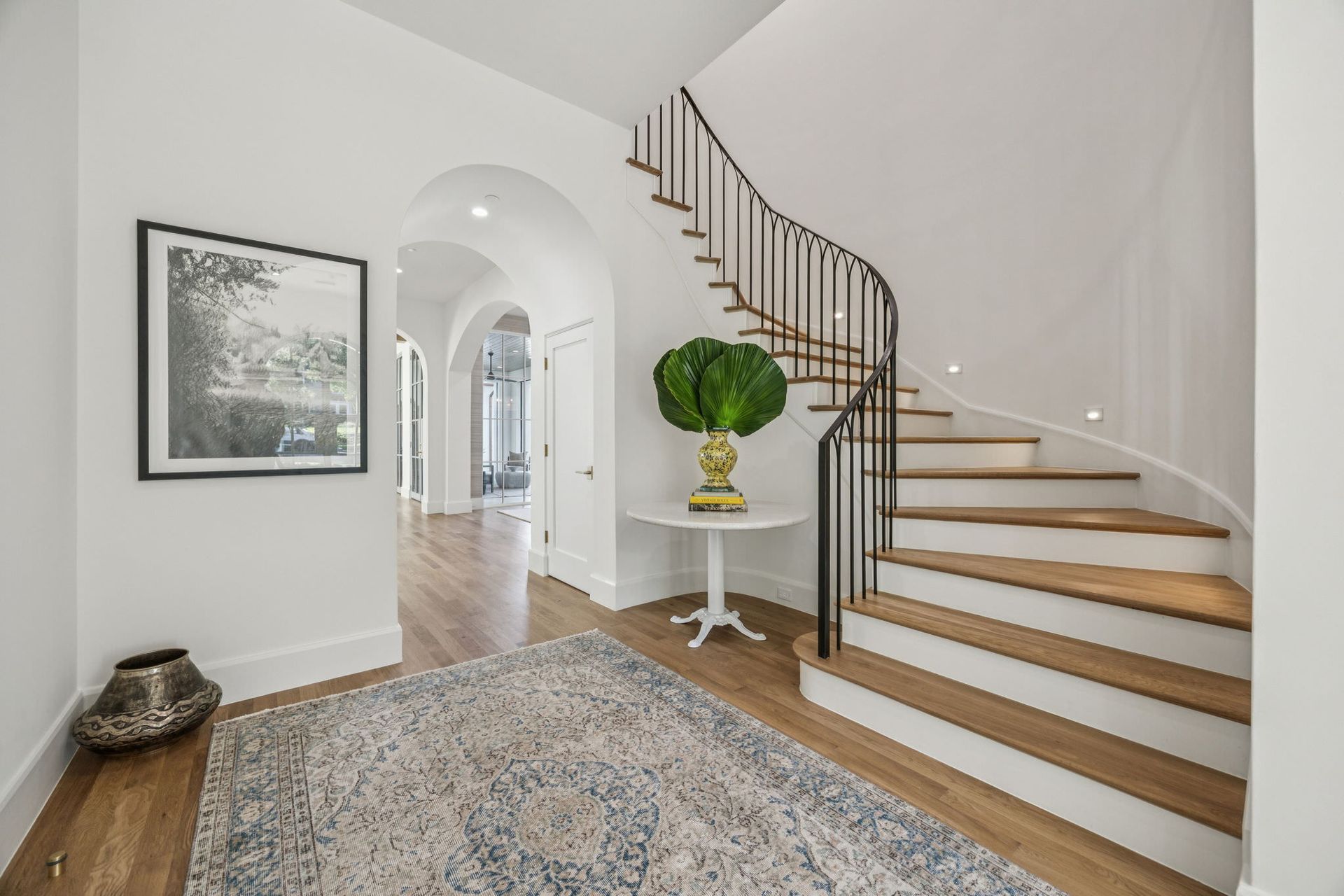 Entryway with curved staircase, hardwood floors, white walls, and a rug.
