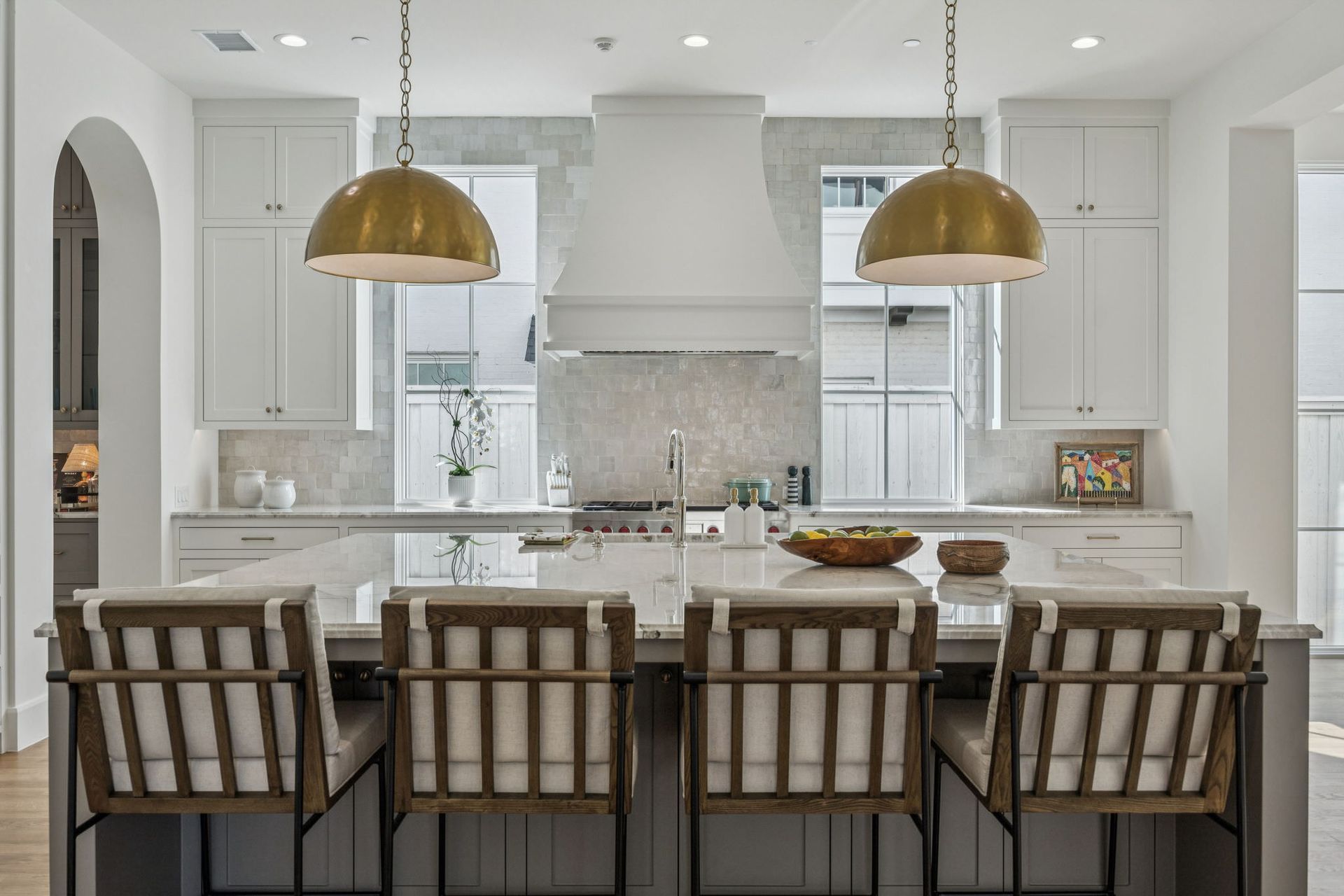 Kitchen with island seating, white cabinets, gold pendant lights, and marble backsplash.