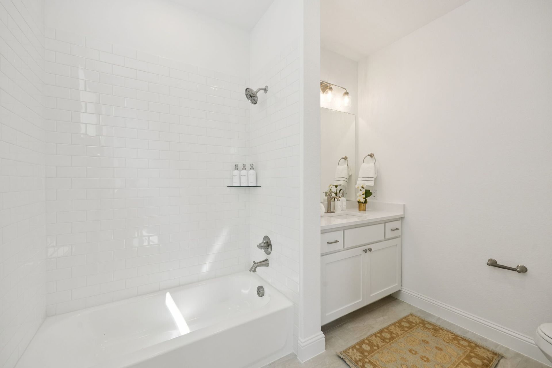 White bathroom with bathtub, subway tile, vanity, mirror, and rug.