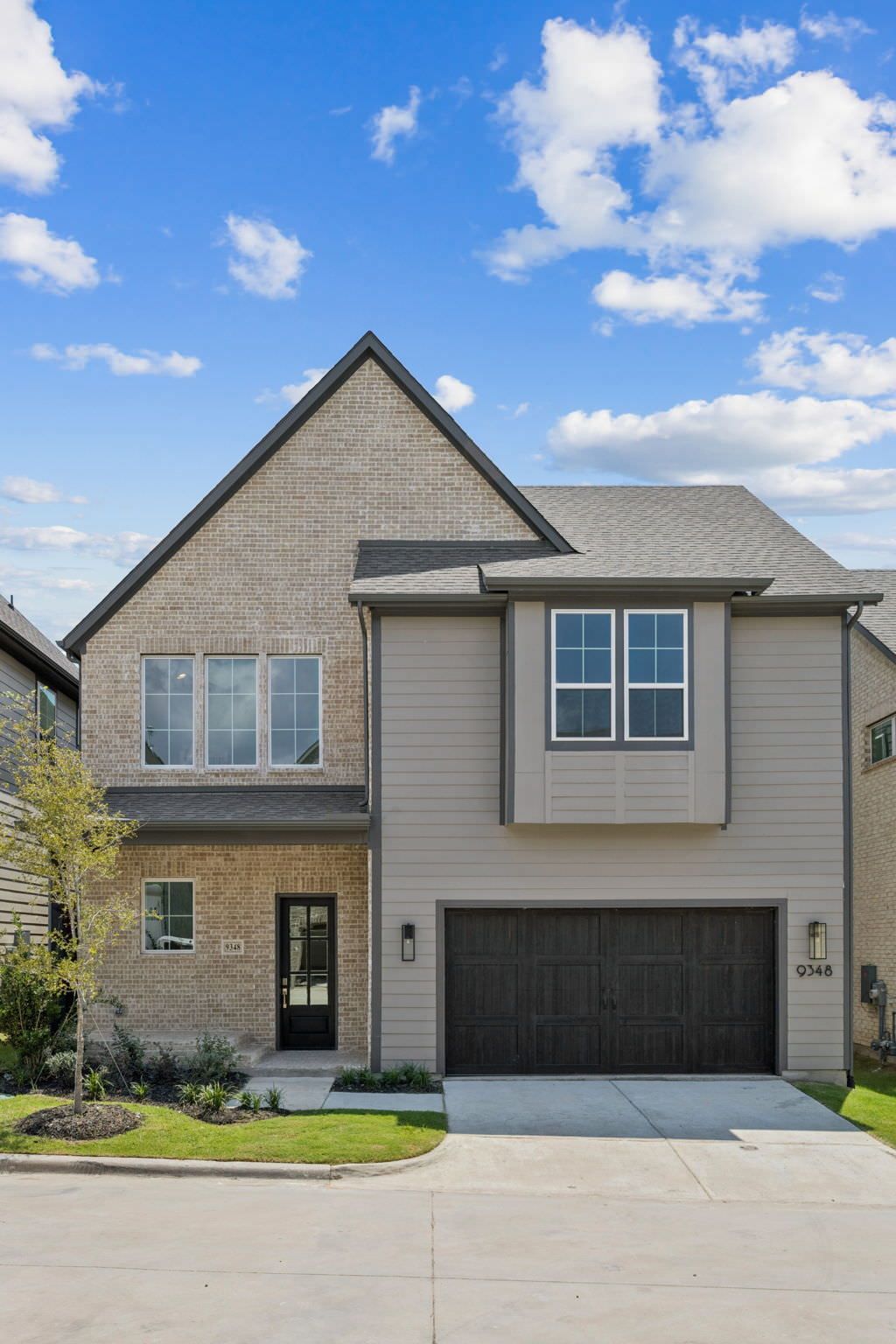 Two-story house with brick facade, gray siding, and a dark brown garage door against a cloudy blue sky.
