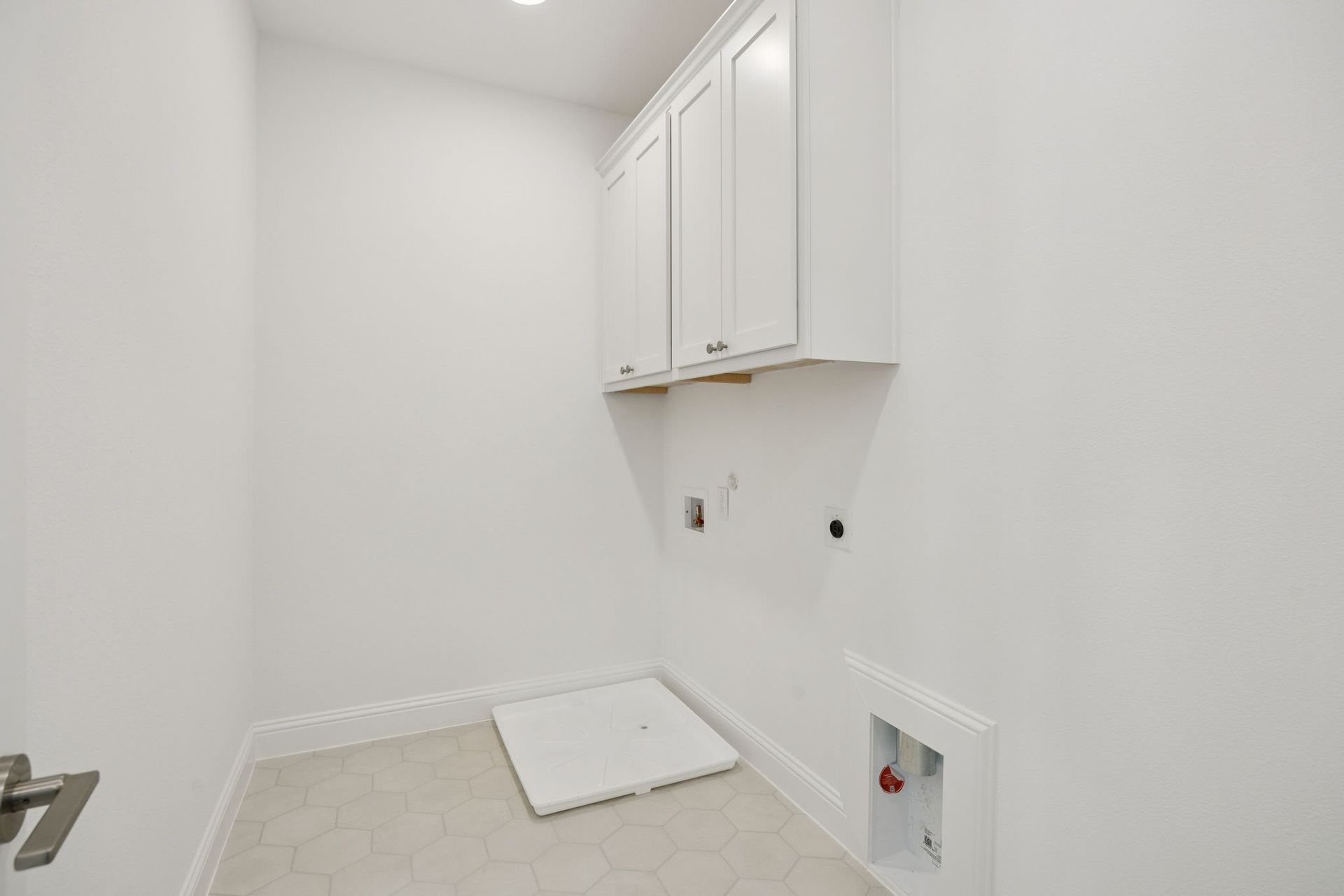 Empty white laundry room with upper cabinets, washing machine connections, and a floor mat.