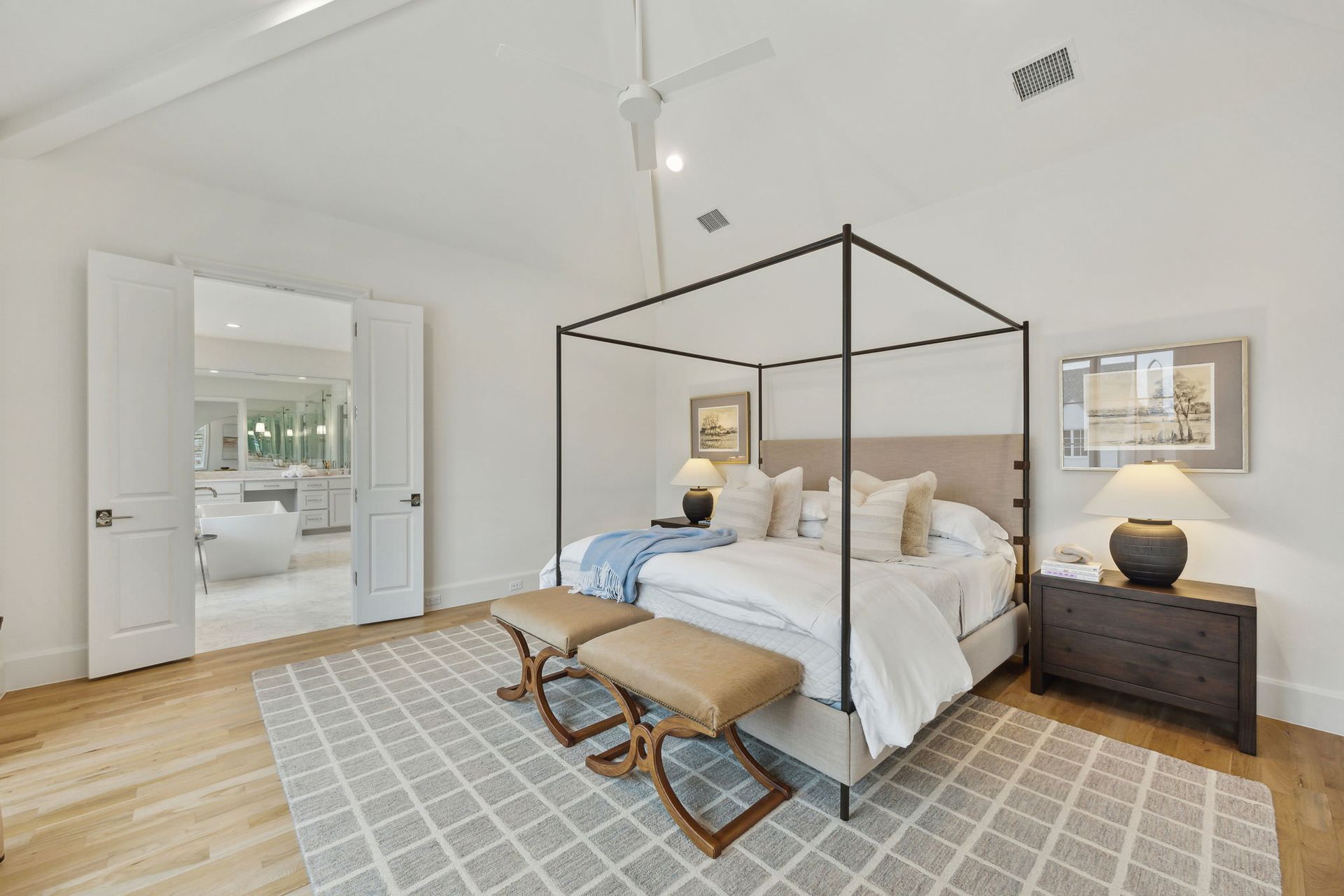 Bedroom with a canopy bed, two benches, nightstand, and doorway to a sitting area.