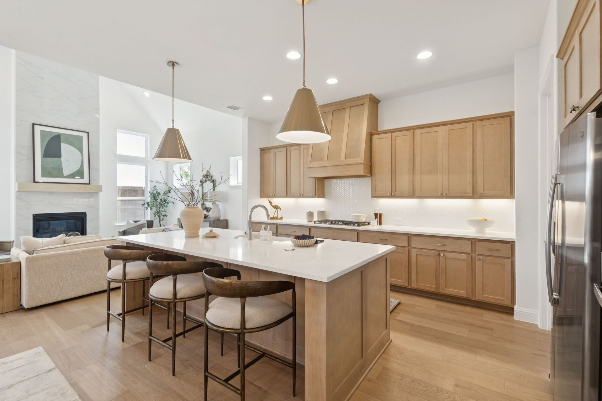Modern kitchen with light wood cabinets, white countertops, and an island with stools.